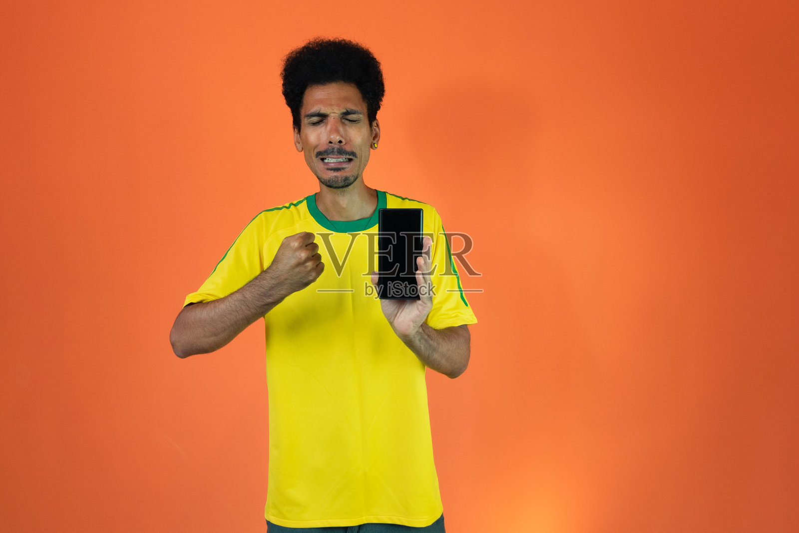 体育迷庆祝手持手机在橙色背景隔离。球迷欢呼雀跃。照片摄影图片