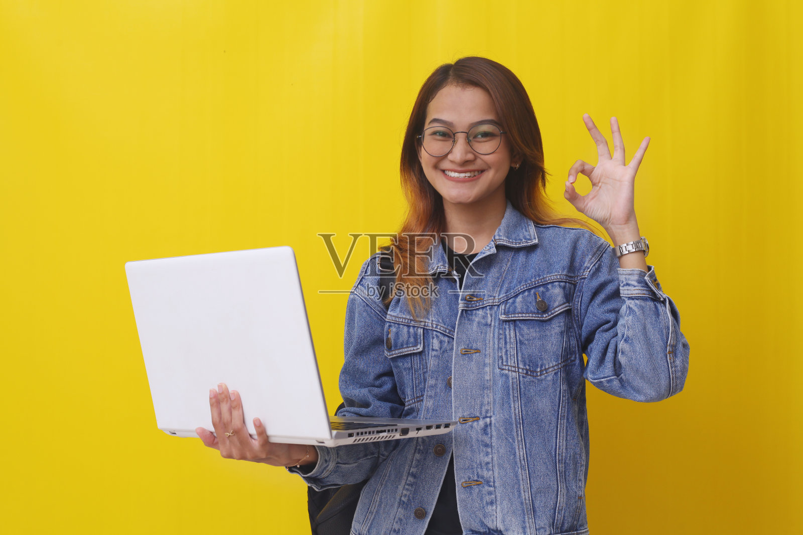 快乐的亚洲年轻大学生站着,用正常的手势拿着笔记本电脑照片摄影图片