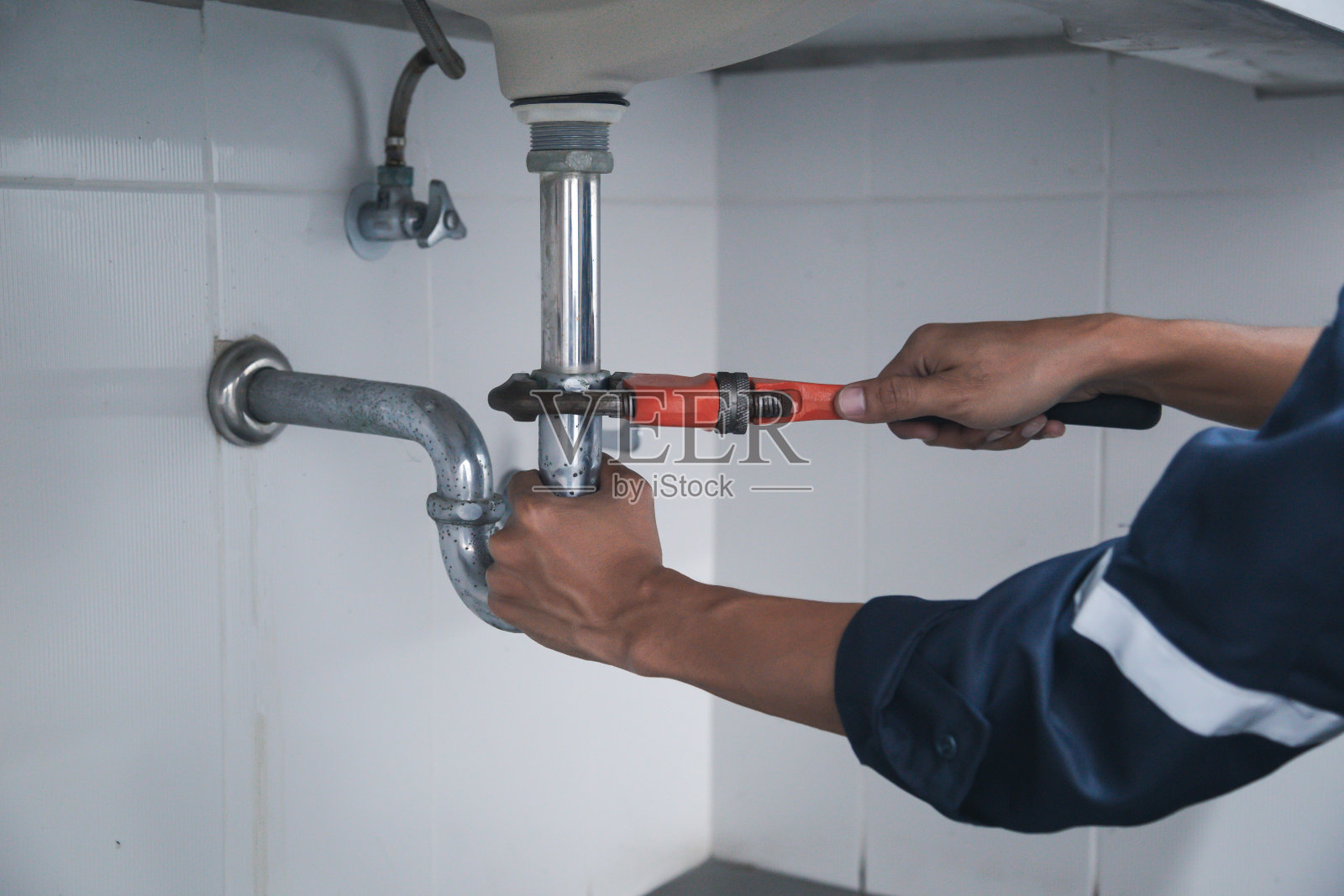 男管道工用扳手修理家庭浴室漏水的水槽。照片摄影图片