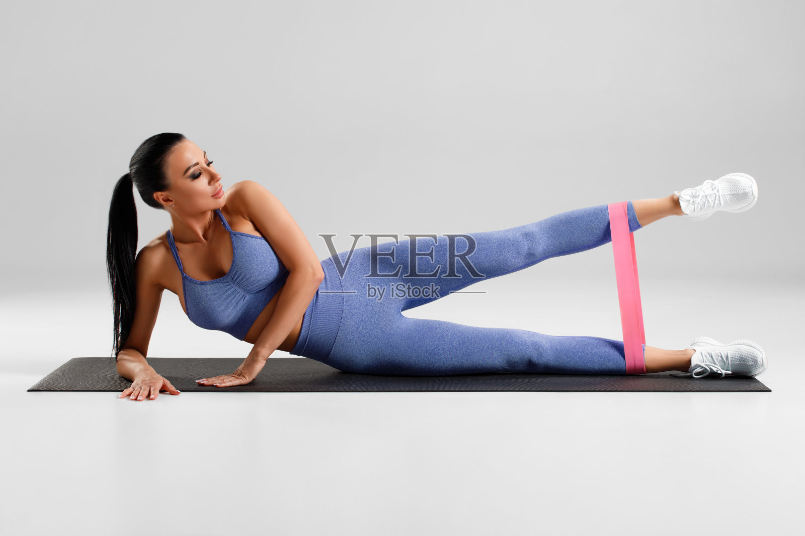 健身女性在做抬腿锻炼臀部与阻力带在灰色的背景。运动女孩在健身照片摄影图片