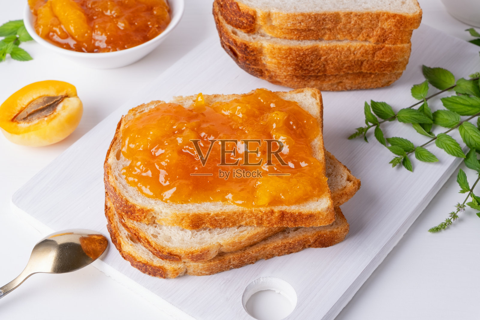 白木桌上放着烤面包、杏酱、新鲜水果和薄荷。美味的早餐照片摄影图片