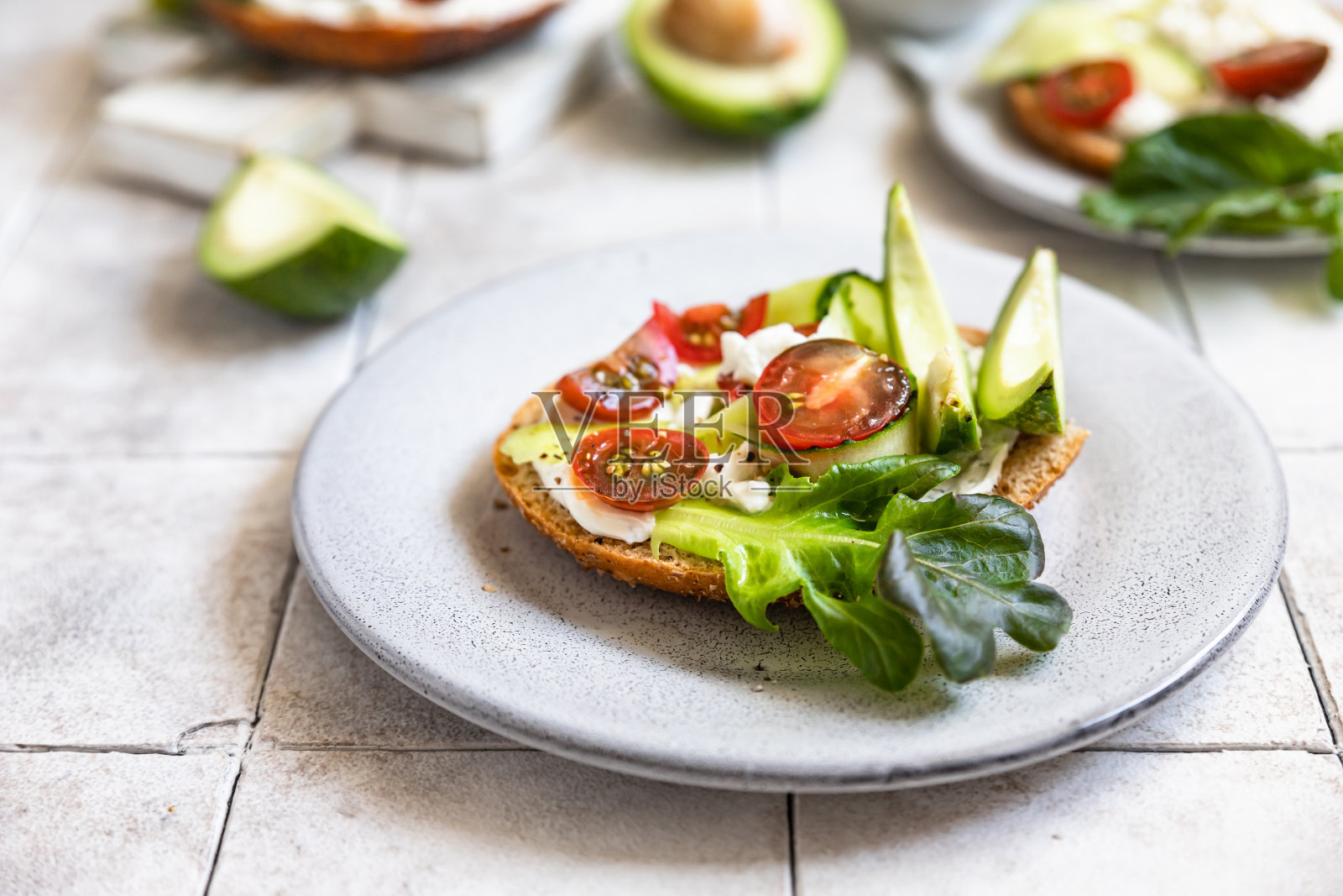 百吉饼三明治,上面有奶油芝士、农家芝士、牛油果、西红柿、黄瓜和沙拉叶。健康的早餐食品。照片摄影图片