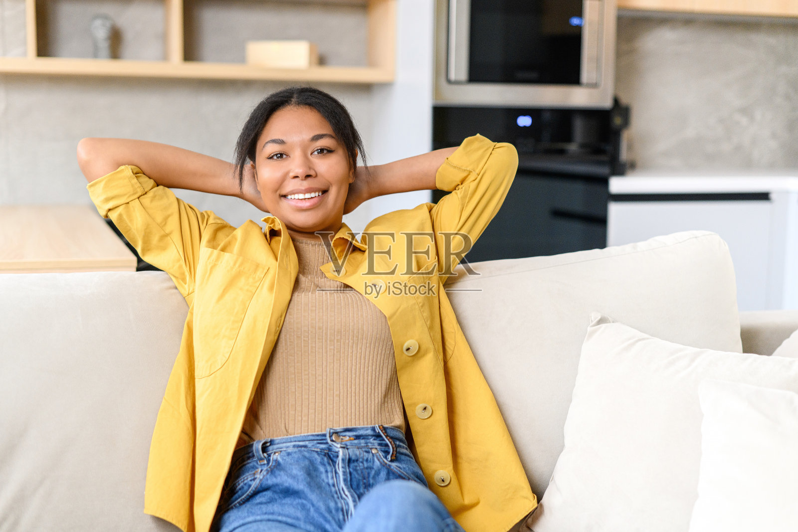 和平安详的多种族女士看着镜头坐在沙发上舒适的客厅,在家里度过周末。迷人迷人的年轻非洲裔美国女性照片摄影图片