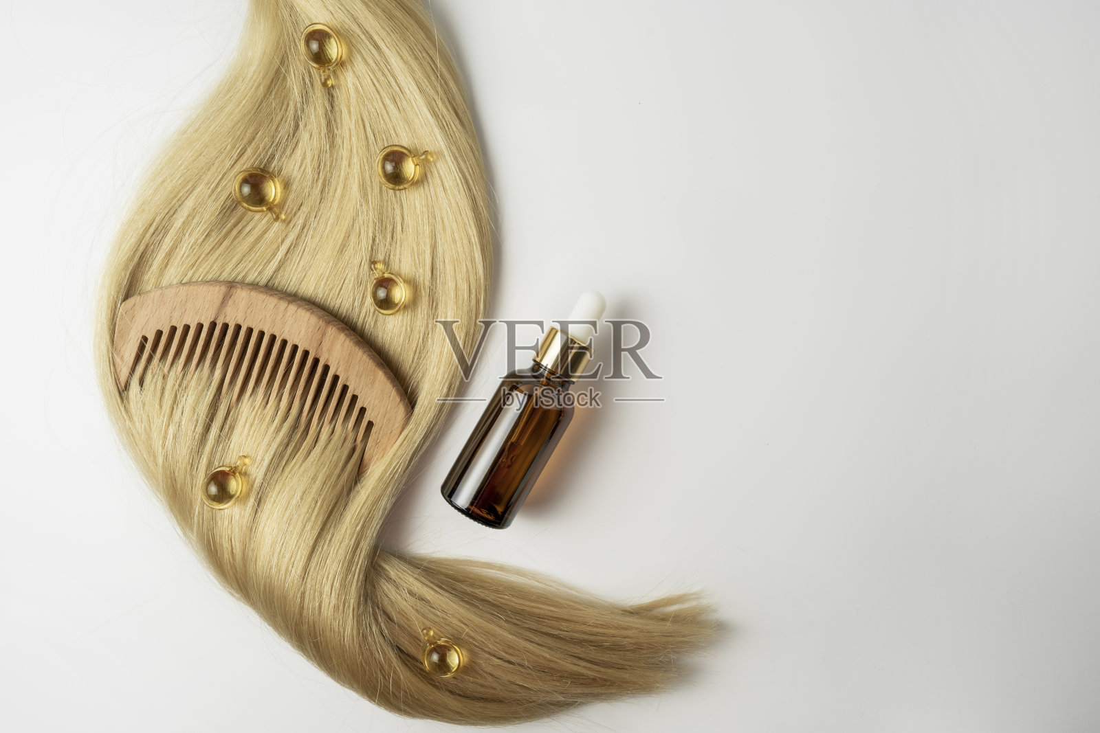 一种天然的护发精油或精华液,装在金色的胶囊里,放在白色的桌子上。头发护理和平滑的概念照片摄影图片