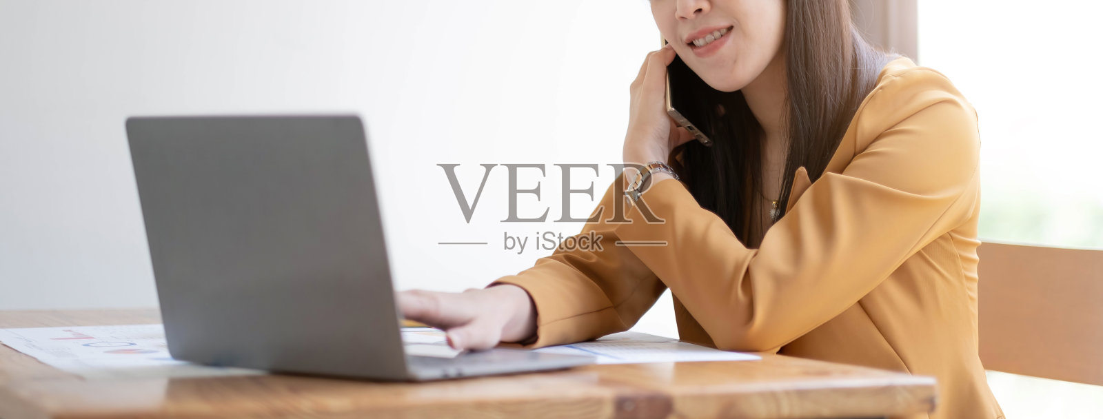 亚洲年轻快乐漂亮的女商人女职员职员正装坐在微笑谈论智能手机电话工作咨询讨论与客户在工作桌上的笔记本电脑。照片摄影图片