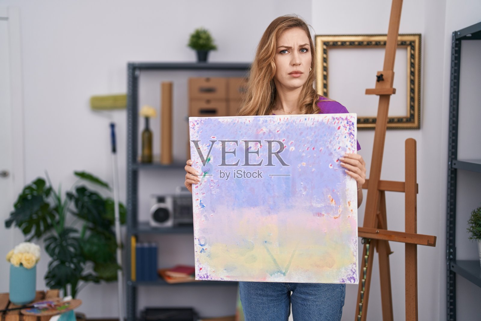 美丽的金发女子拿着油画画布,表情茫然而困惑。怀疑的概念。照片摄影图片