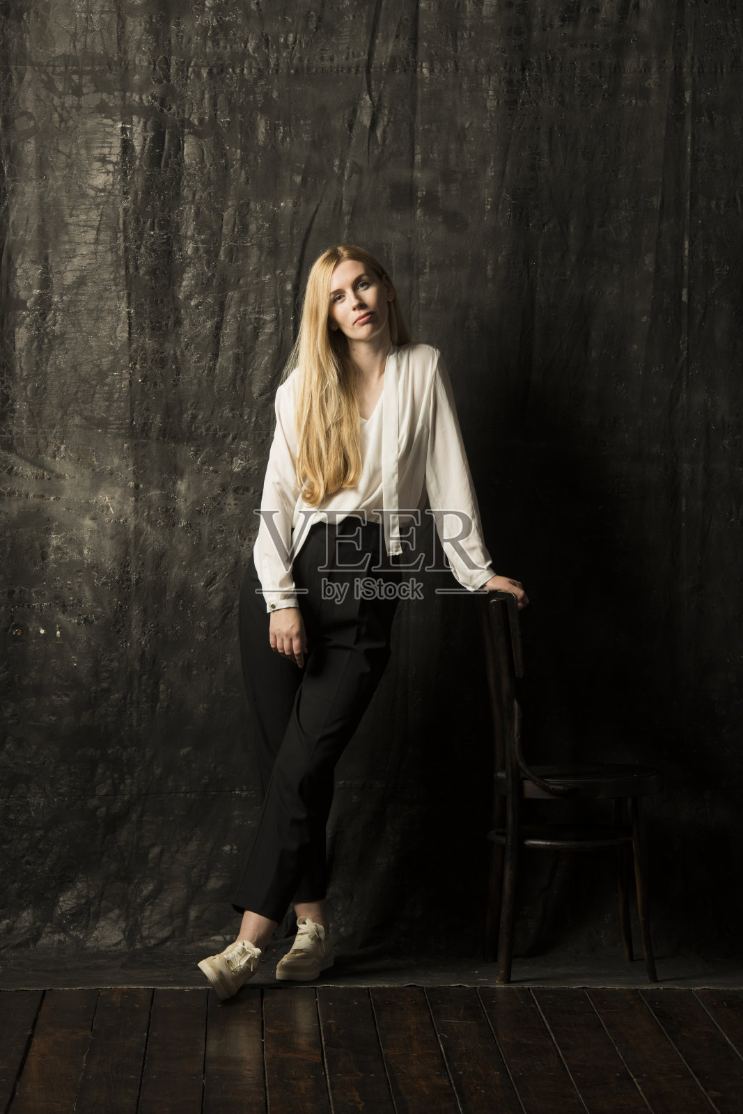 一个美丽的金发女人的肖像,一头长发,白色衬衫和黑色裤子在灰色孤立的背景。一个迷人的女孩在黑暗的背景上摆姿势。照片摄影图片