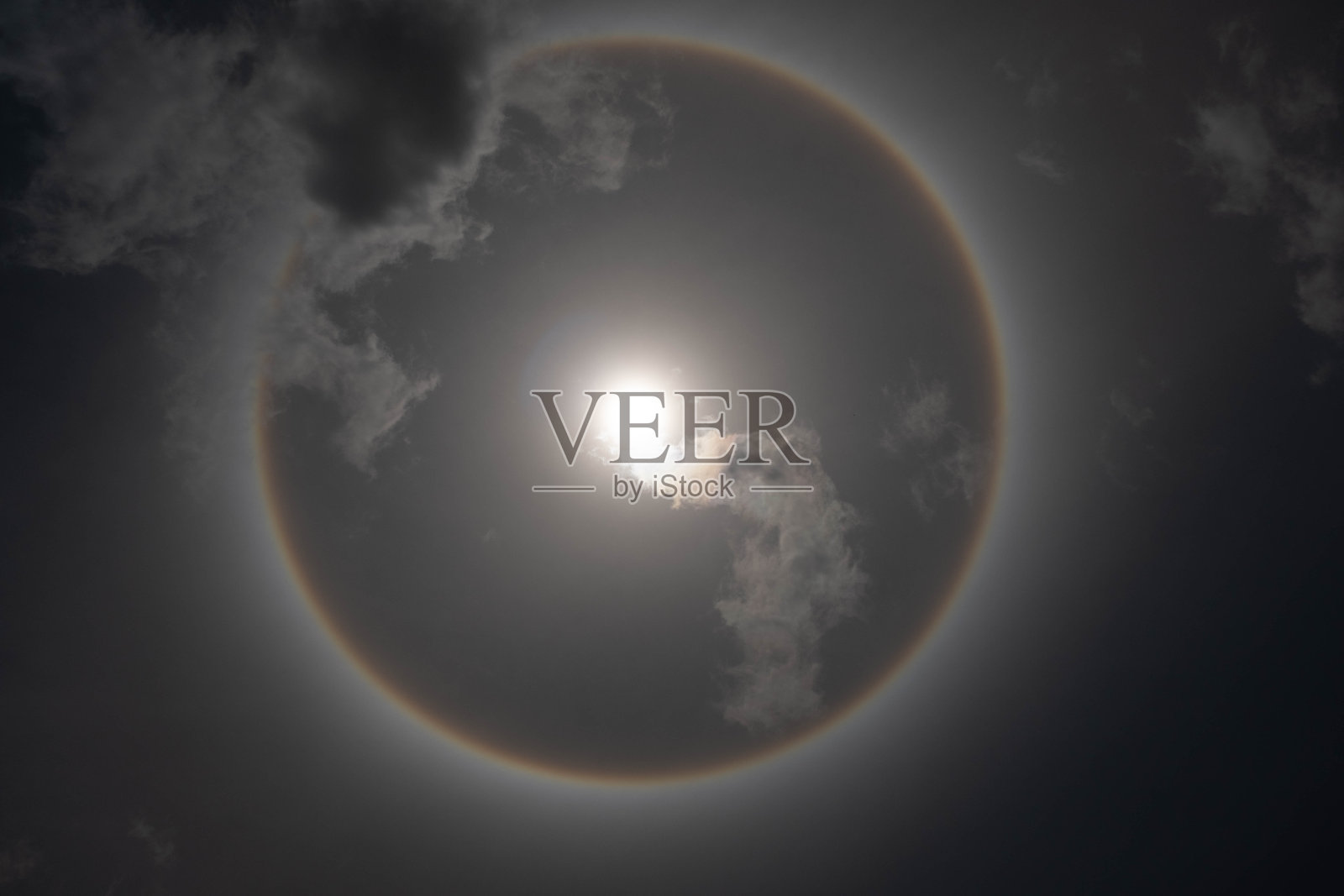 美丽的太阳用一道圆形的彩虹包围着明亮的天空和白云。现象,太阳光环。照片摄影图片