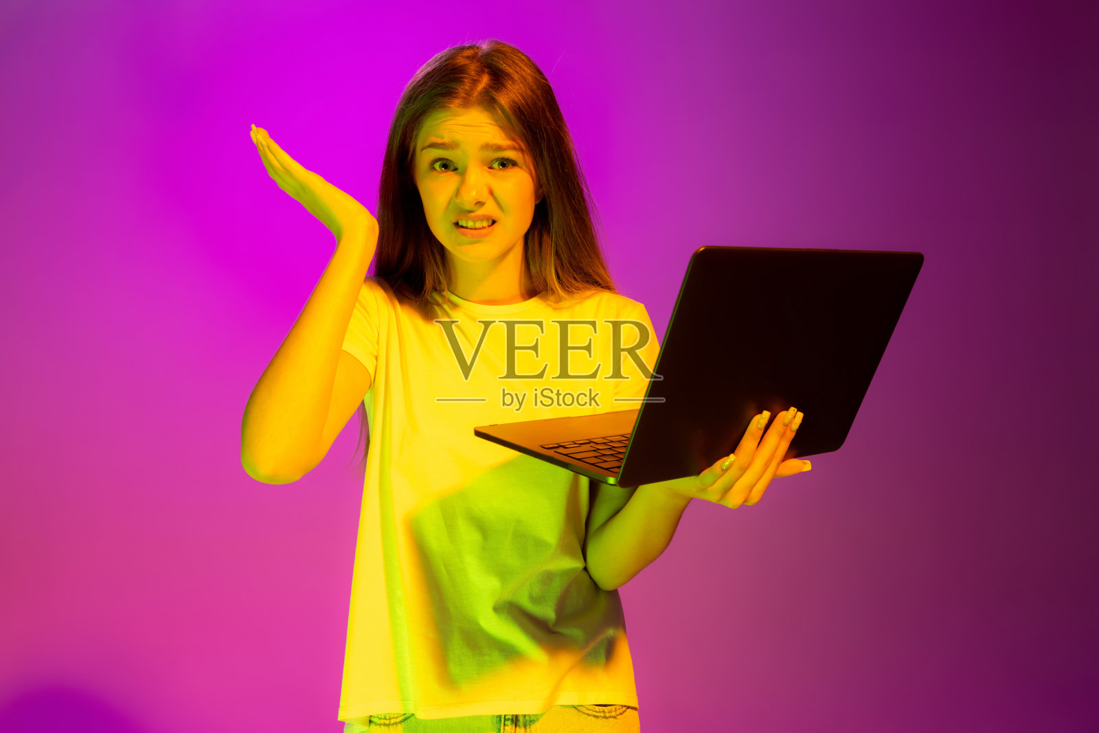 年轻女孩的肖像,学生通过在线考试的笔记本电脑隔离在粉红色的背景下的霓虹灯照片摄影图片