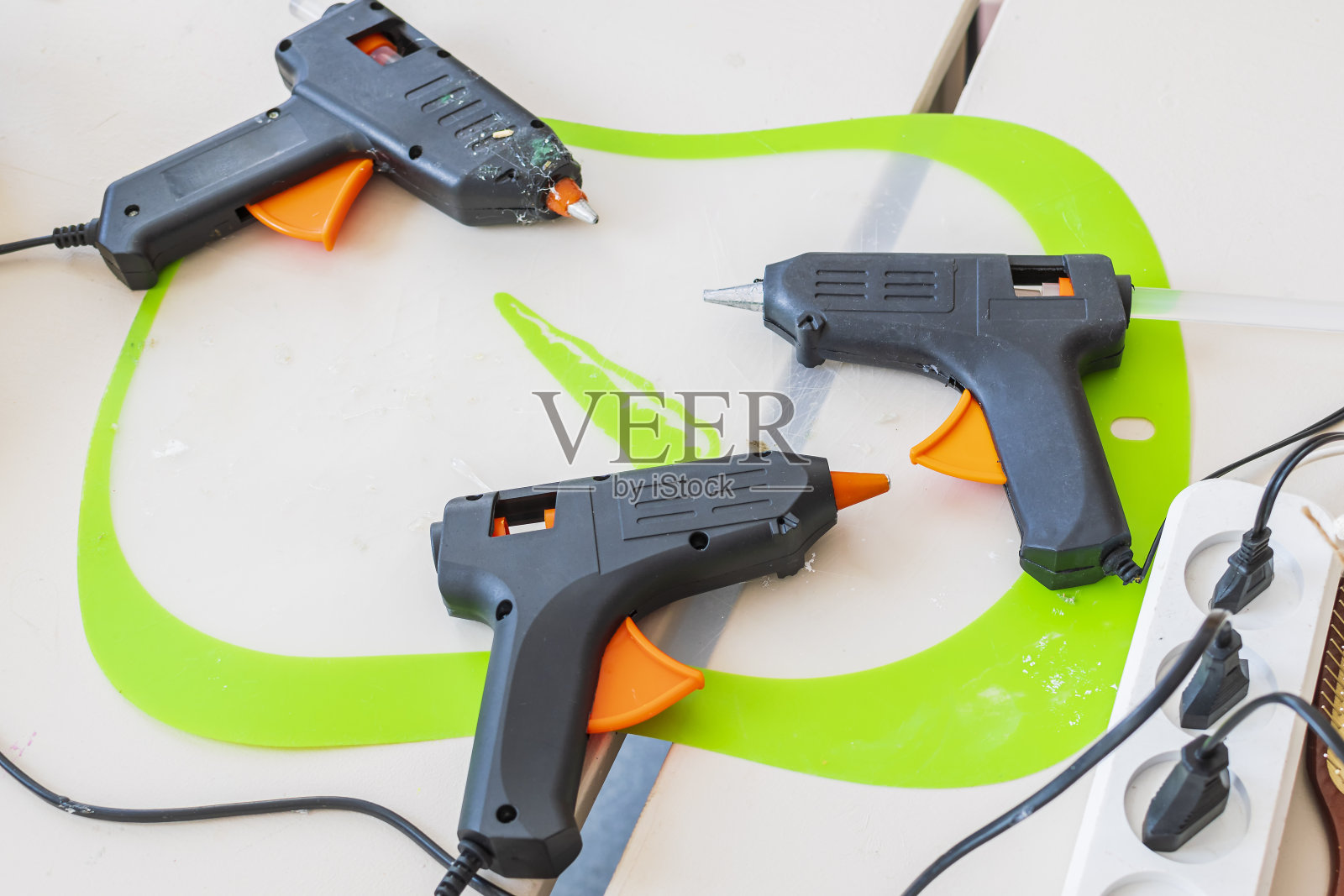白色的桌子上放着三把接在电源插座上的塑料胶枪。装饰艺术的工具。照片摄影图片