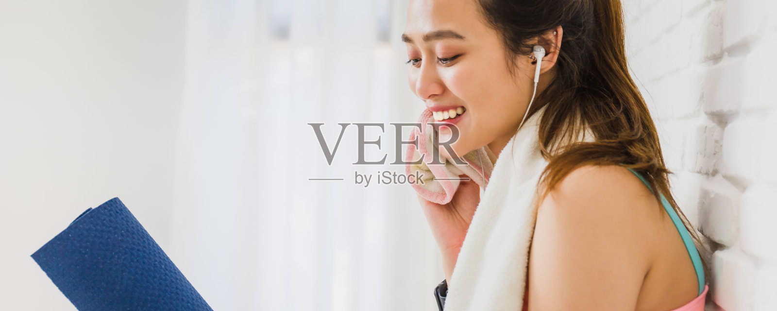 亚洲美女休息和抱着瑜伽垫玩瑜伽和锻炼后,在白色砖墙背景与副本空间。运动减肥,增加灵活性和收紧形状。照片摄影图片