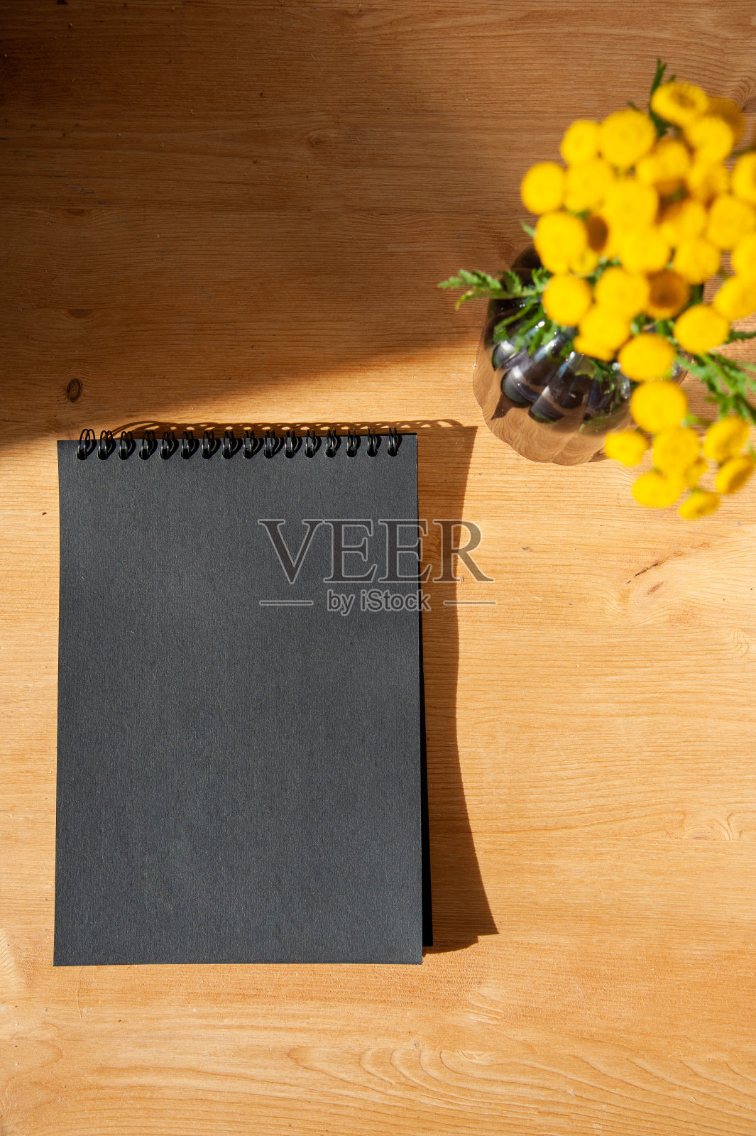 唐茜花插在花瓶里,放在桌子上一个黑色笔记本旁边照片摄影图片