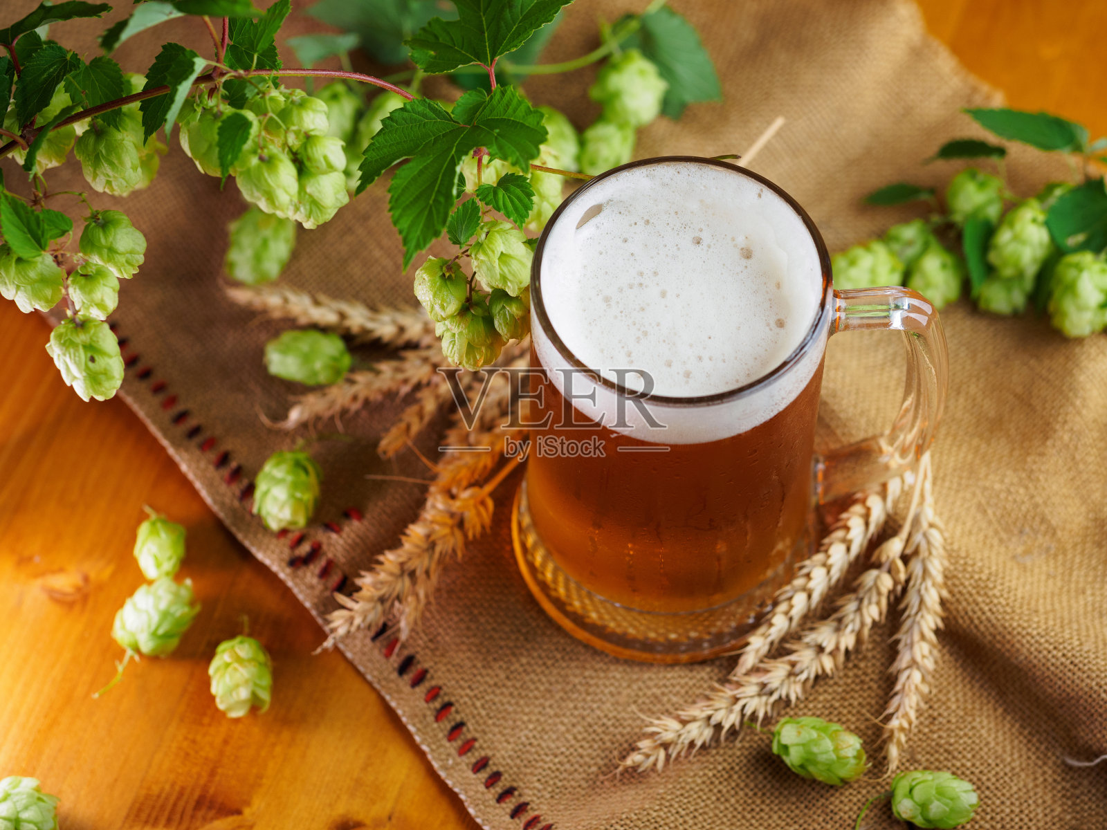 木桌上放着一杯清淡的啤酒,绿色的啤酒花和成熟的小麦穗。照片摄影图片