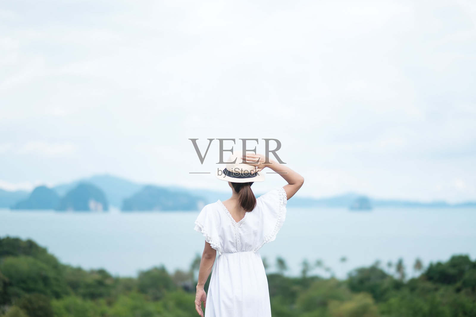 快乐的旅行者白衣女子享受美丽的景色,独自游客与帽子站立和放松的海洋。旅游、暑假和度假的概念照片摄影图片