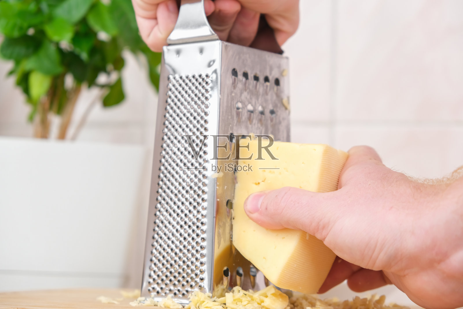一名男子在金属刨丝器上摩擦奶酪,以冷冻和进一步烹饪披萨、意大利面。照片摄影图片
