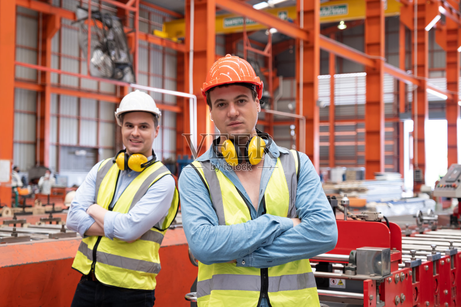 择优关注白人男性机械工程师,穿戴安全装备。同时负责厂区内机器的维护和安全控制。带有模糊背景的重型机械。照片摄影图片