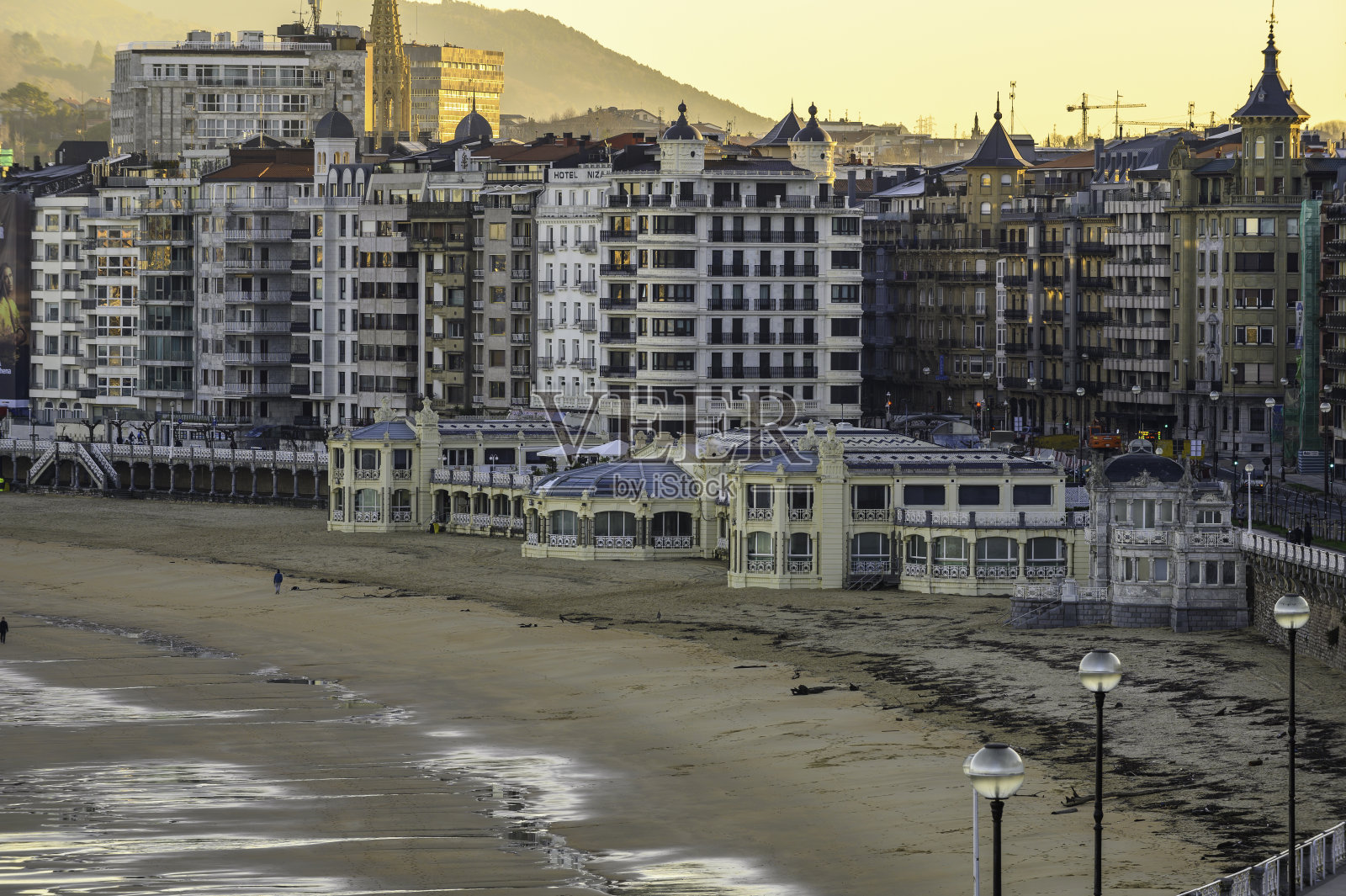 圣塞巴斯蒂安贝壳湾珍珠的特写。海滩上的沙子被低潮浸湿了,在城市的建筑背后你可以看到黎明的黄光照片摄影图片