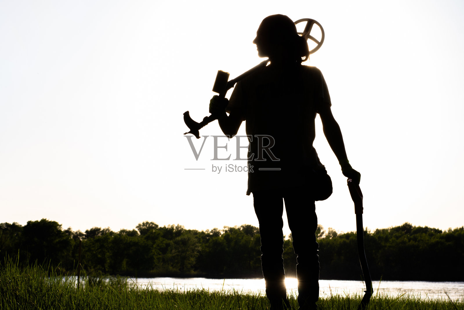 一个男人的剪影他的肩膀上有一个无线金属探测器另一只手拿着铲子。照片摄影图片