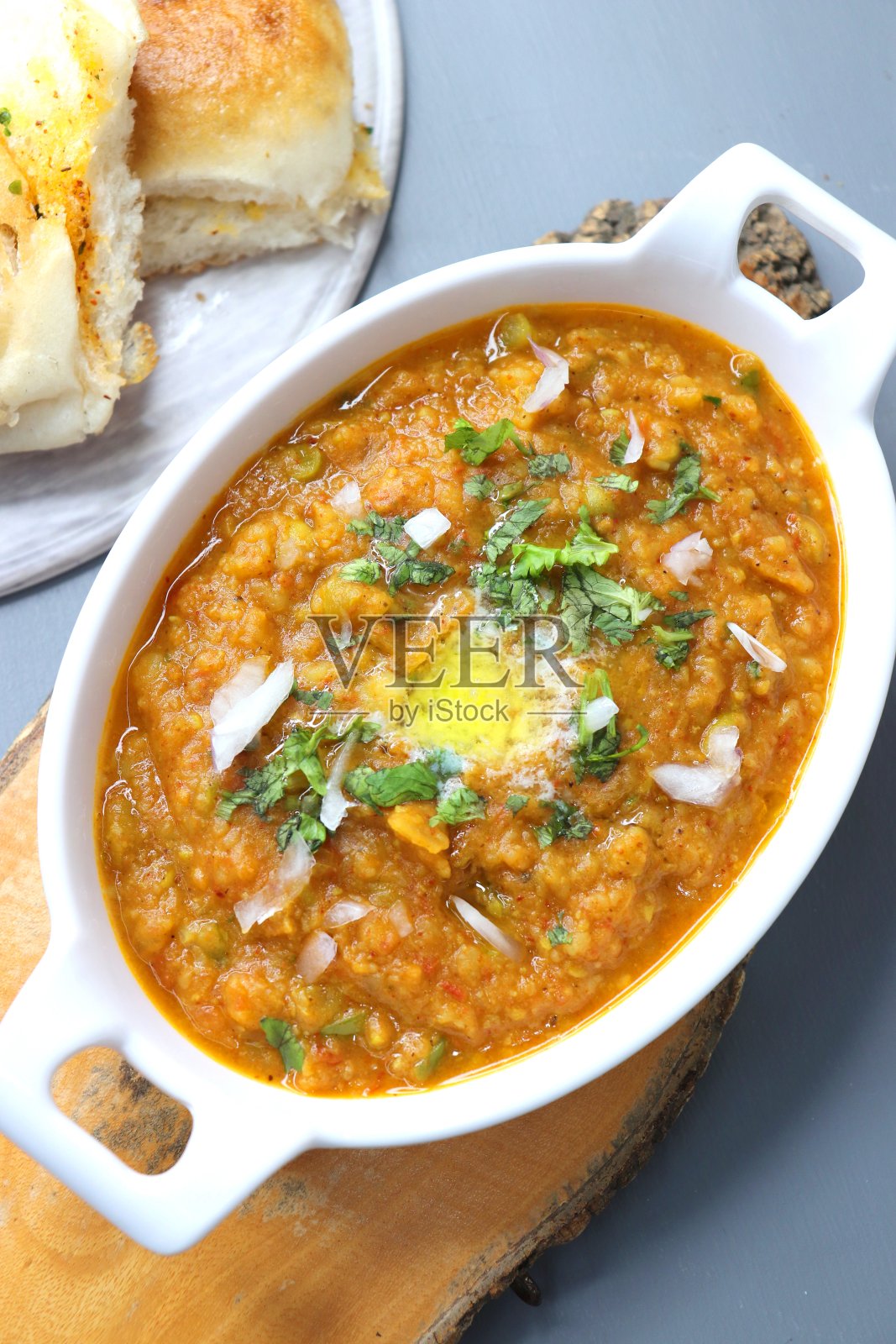 印度孟买街头风格的Pav Bhaji,用豌豆,生洋葱,香菜和黄油装饰。辛辣的厚咖喱混合蔬菜与铺在白色背景与复制空间。照片摄影图片