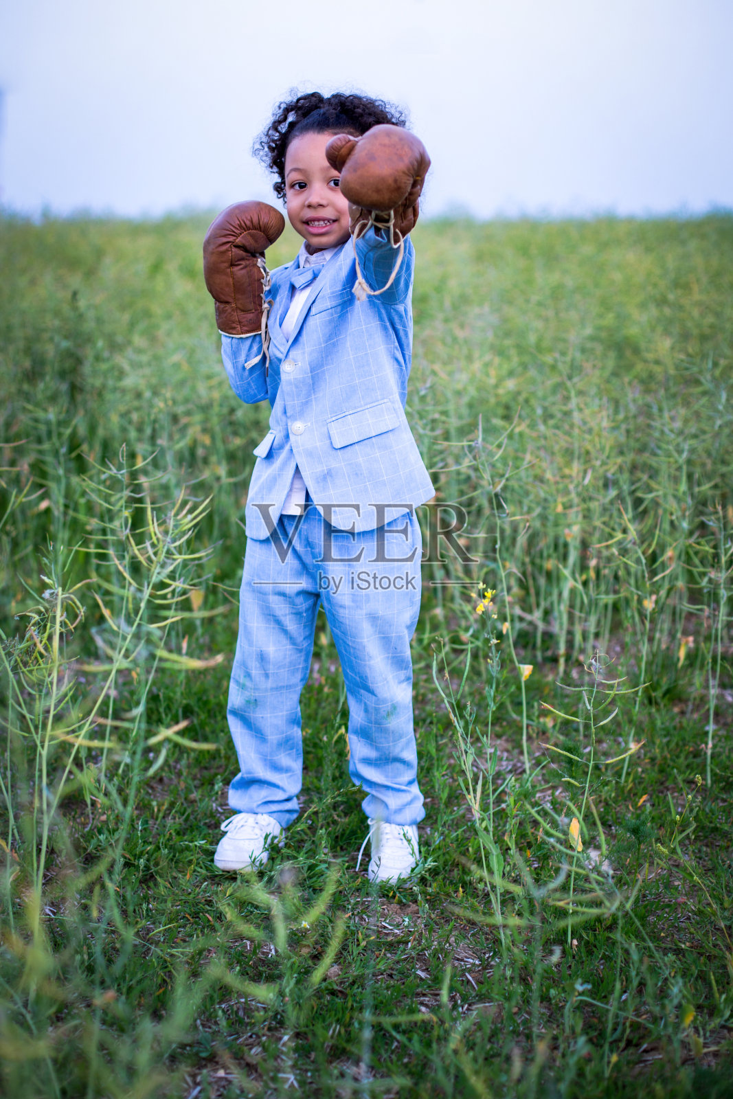 穿着蓝色西装戴着拳击手套的黑人小男孩站在田野里照片摄影图片