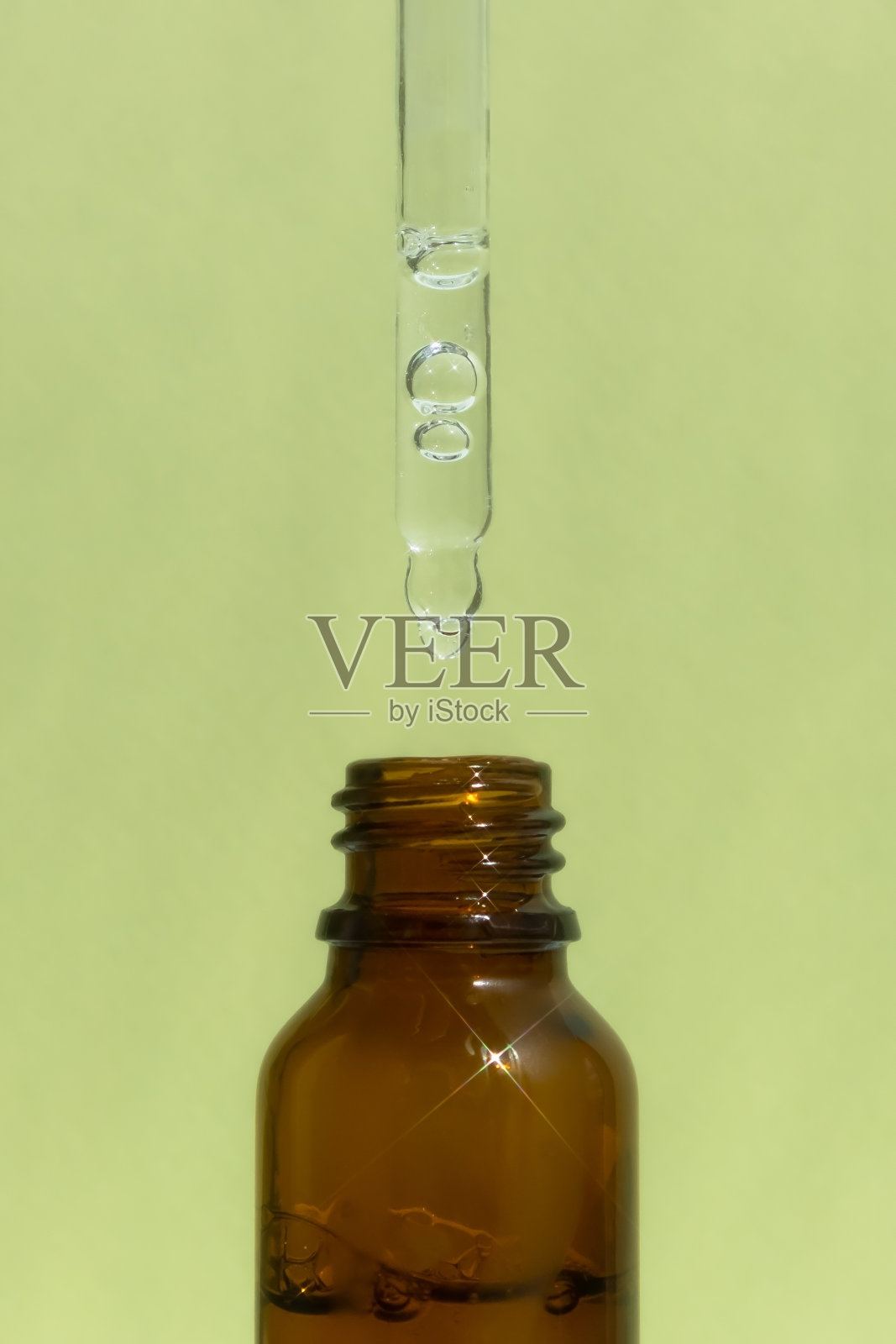 一瓶深琥珀色的玻璃,上面有精华液或凝胶,在绿色的背景上有吸管。玻尿酸化妆品。前视图。照片摄影图片