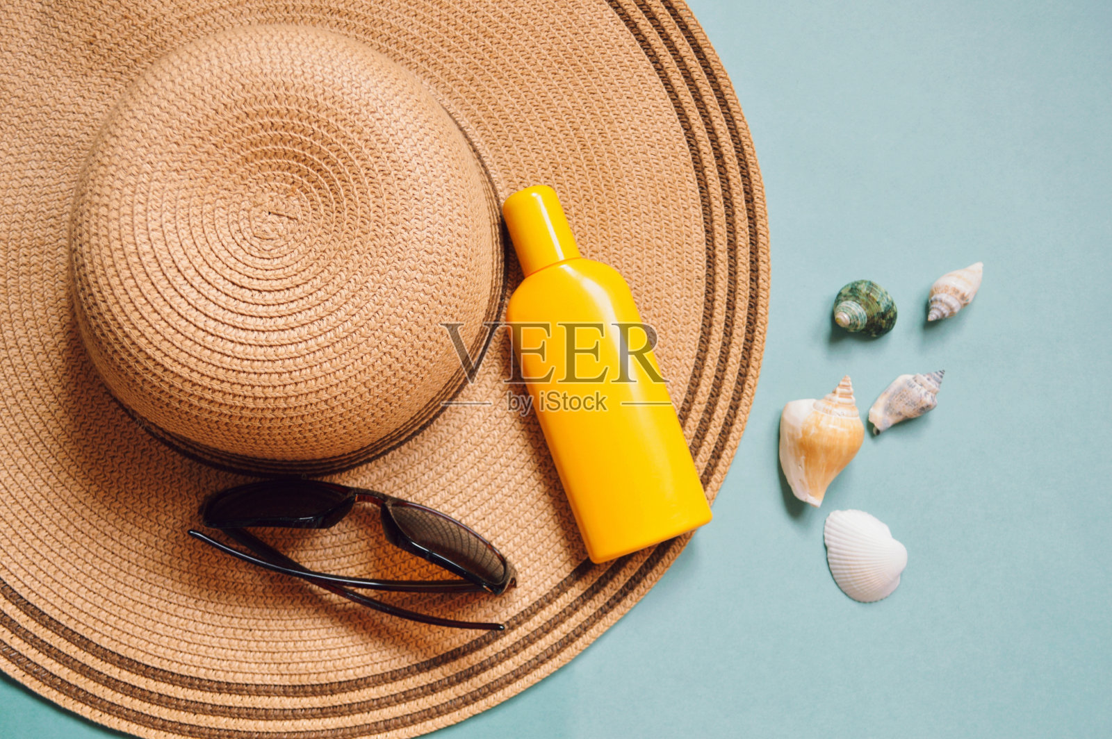 夏日沙滩必备品,海上旅行理念。太阳帽、墨镜、黄色防晒瓶和海贝平铺摄影照片摄影图片