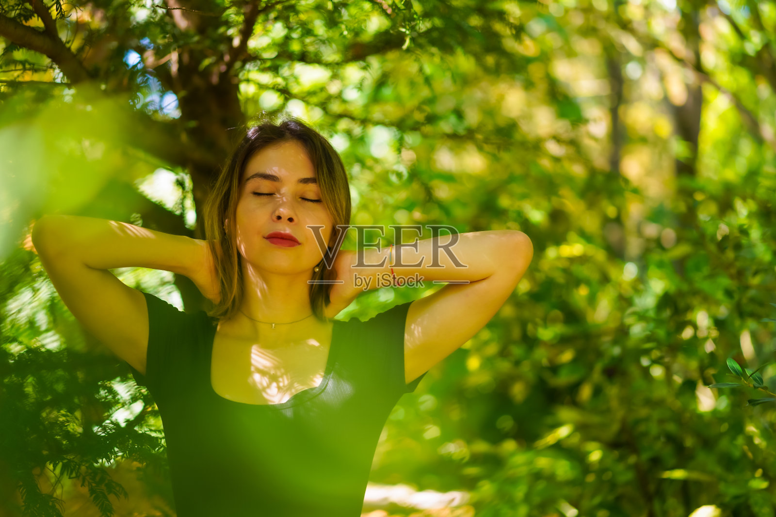 一个年轻的黑发女子在自然的公园里,自由自在,闭着眼睛做梦照片摄影图片