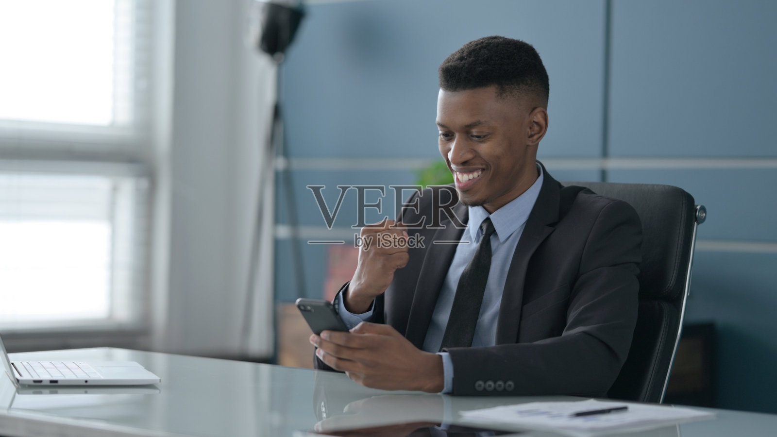 成功的非洲商人用智能手机庆祝成功照片摄影图片