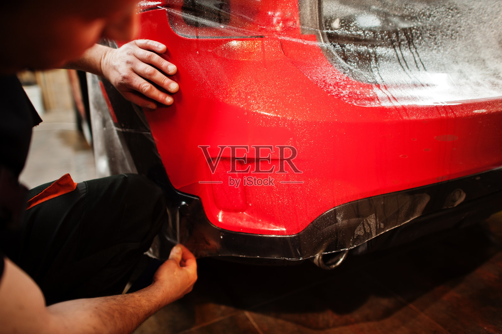 在汽车车间,汽车服务人员在一辆红色车体上涂防石膜。用特殊薄膜保护汽车。照片摄影图片