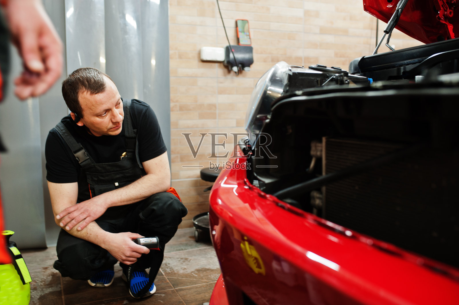 在汽车车间,汽车服务人员在一辆红色车体上涂防石膜。用特殊薄膜保护汽车。照片摄影图片