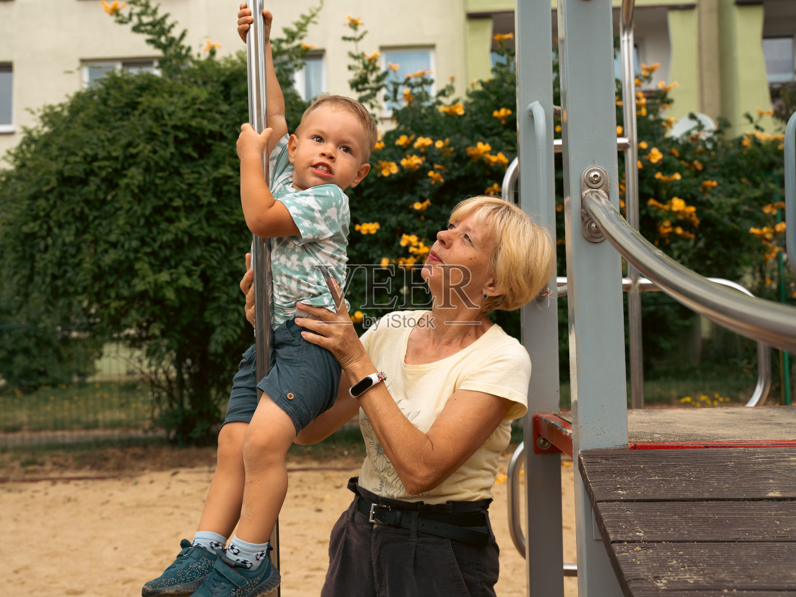 在儿童游乐场,奶奶抱着2岁的孙子。奶奶和孩子玩得很开心。支持童年的象征。阳光明媚,夏天照片摄影图片