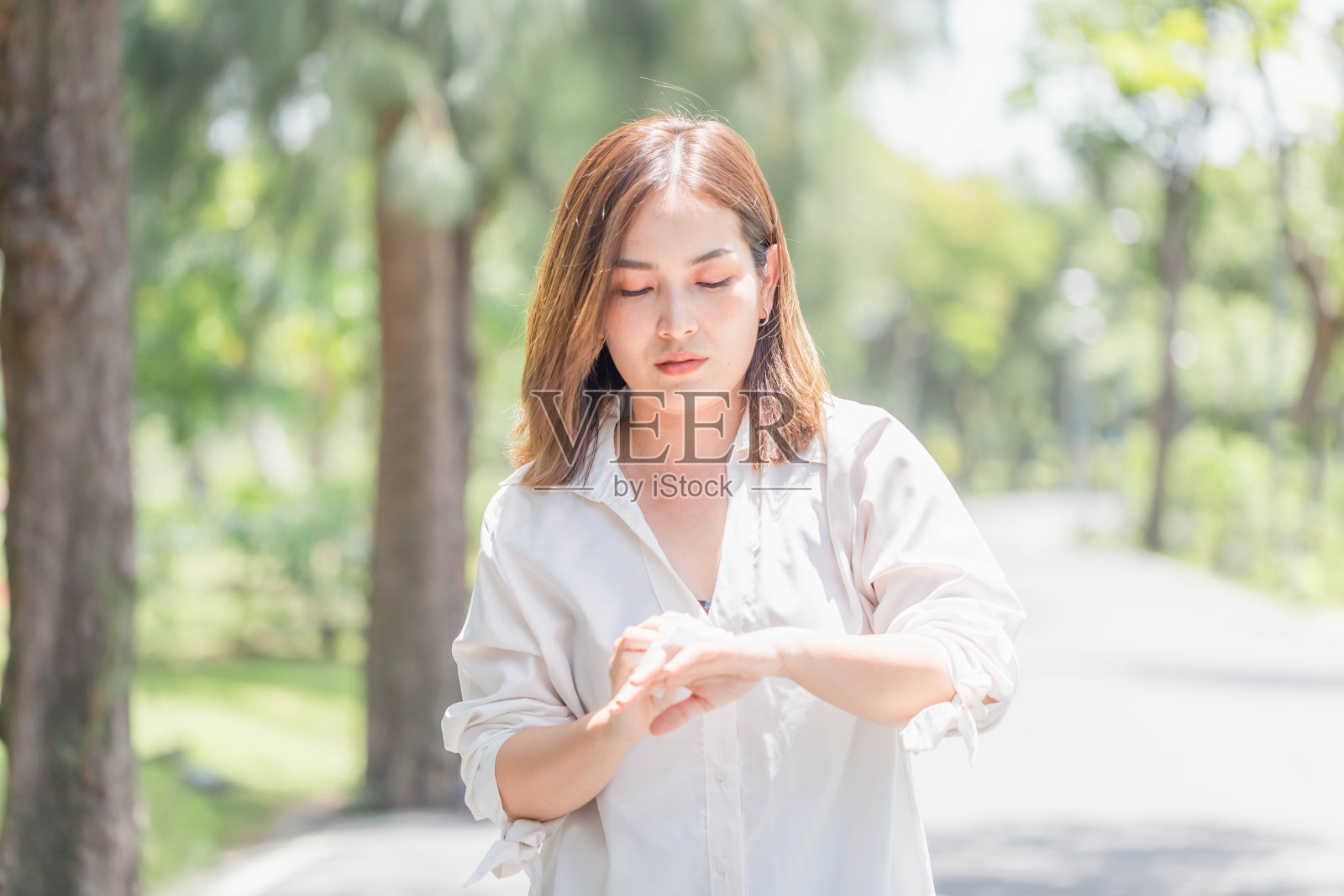 年轻漂亮的女孩在一个温暖的夏天在公园里用纸巾擦汗,在公园里的女人在夏天炎热的天气中暑照片摄影图片