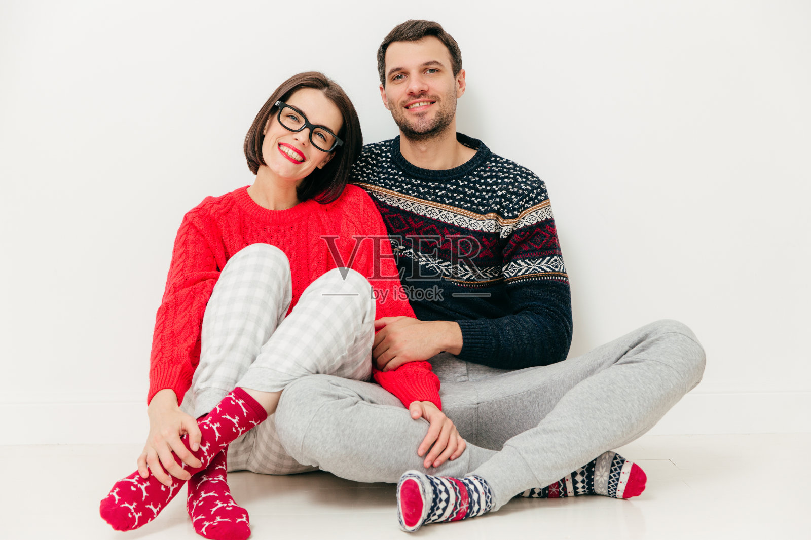 在白色的摄影棚背景下,一对幸福的恋人坐在一起,穿着休闲的衣服,在家享受闲暇时光。可爱的年轻女性和男性伴侣脸上有愉快的微笑照片摄影图片