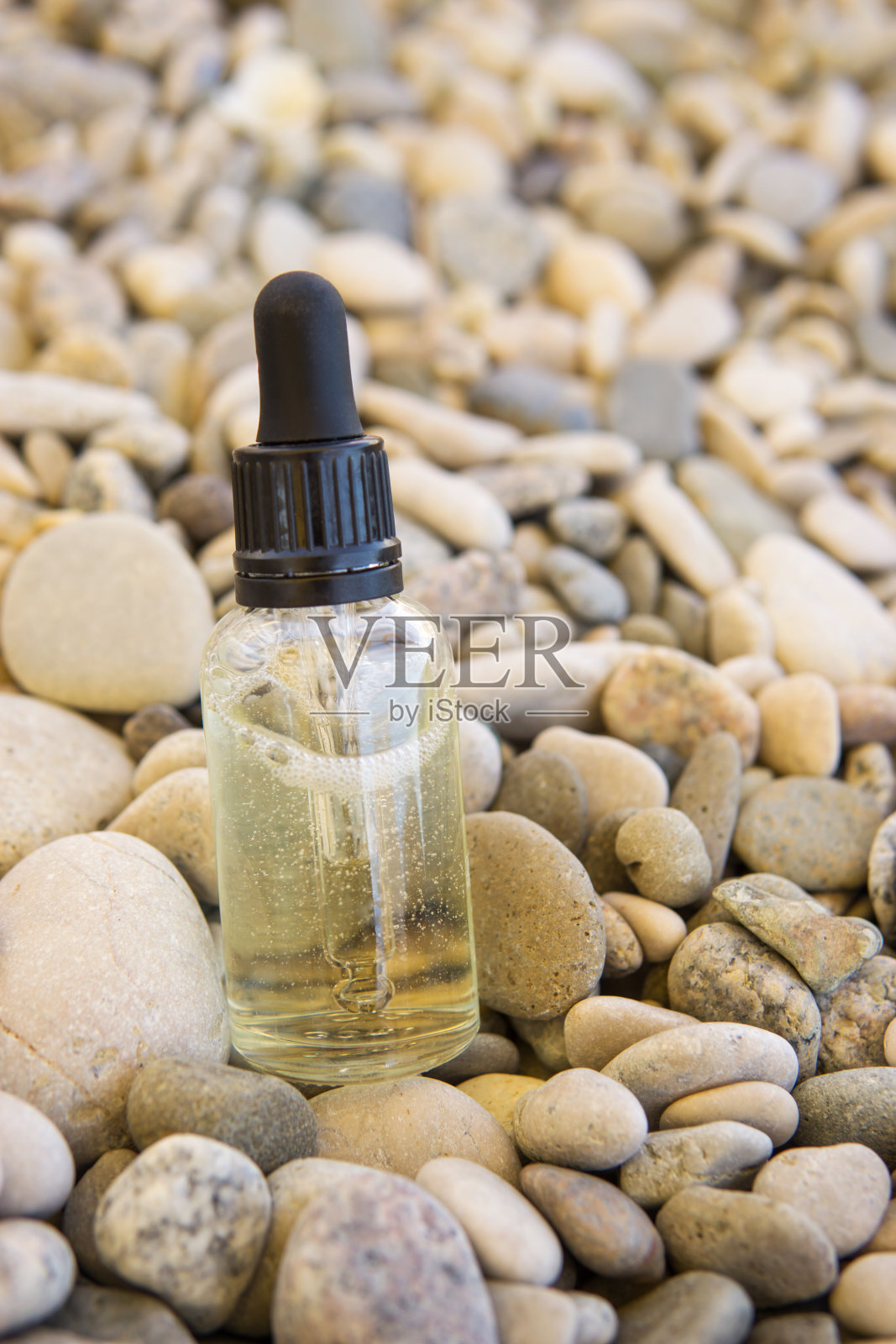 装在玻璃瓶里的化妆品精华液,用吸管吸在石头上照片摄影图片