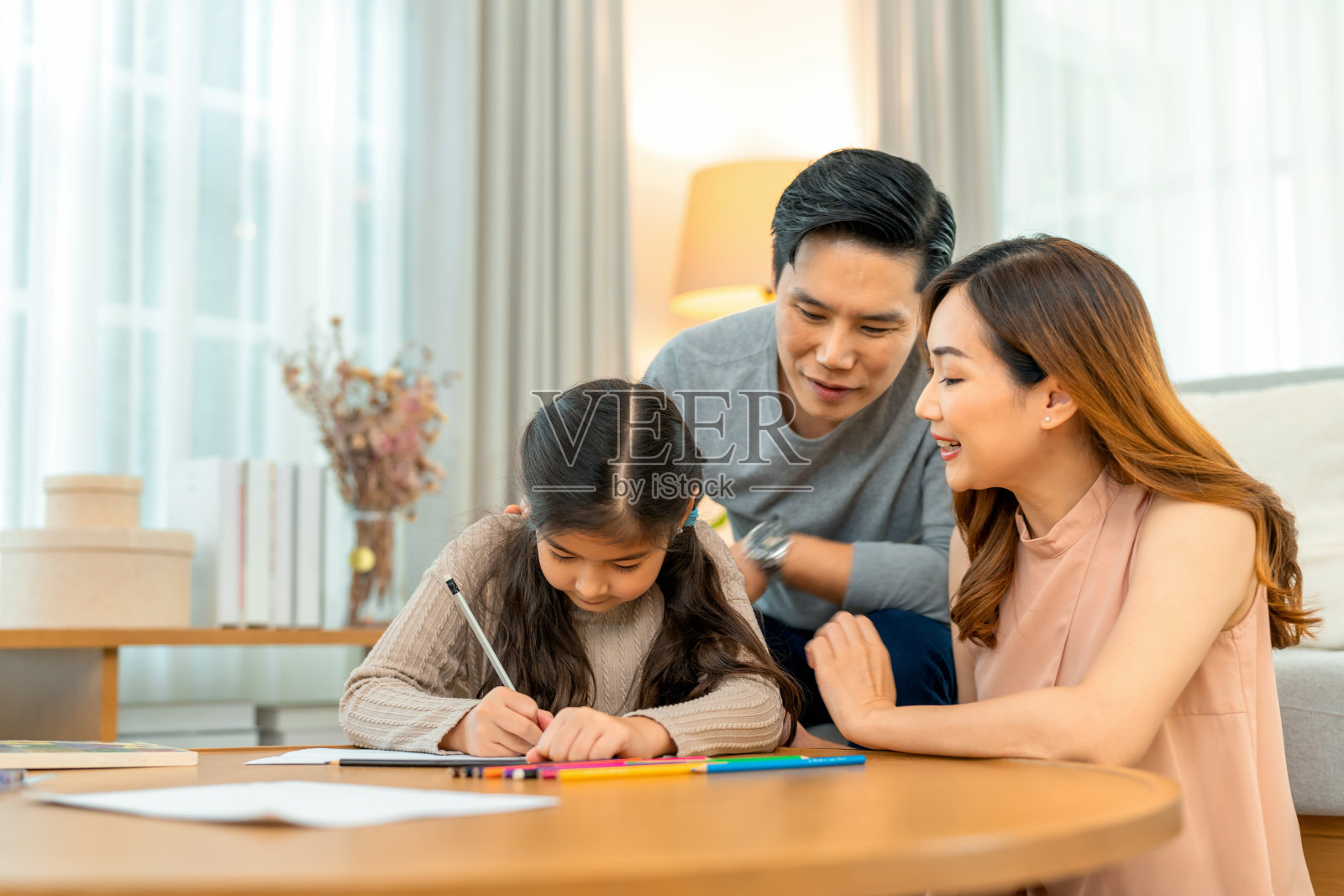 一对幸福的家庭夫妇和他们的女儿坐在沙发前,他们看着女儿在客厅画画和写作的活动。照片摄影图片