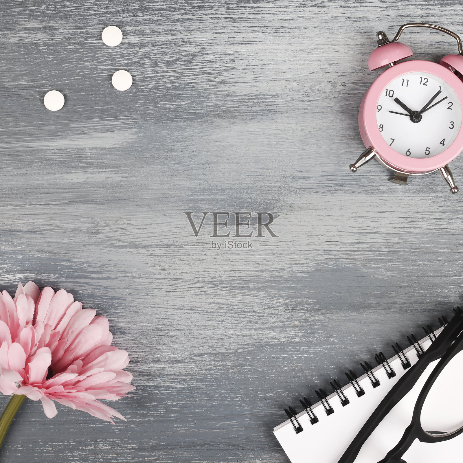 女性健康的概念。医药、保健风格。副本的空间。白色药丸,花,笔记本,眼镜和时钟的蓝色木制背景。广场照片摄影图片