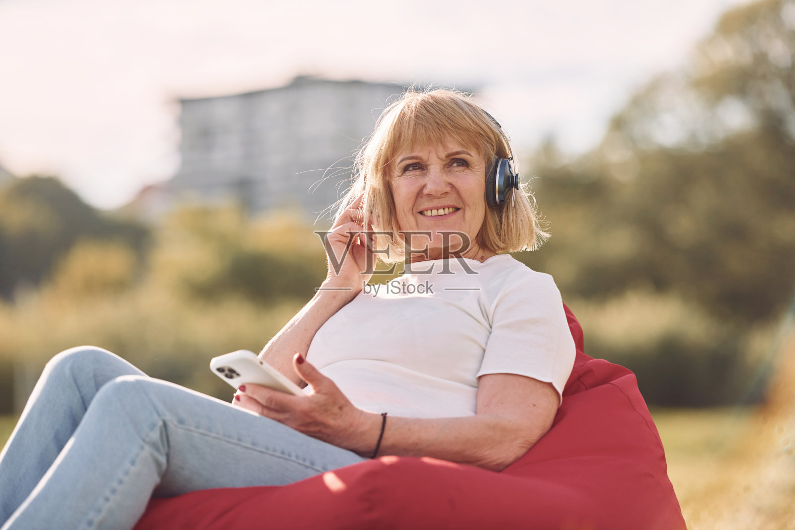 坐在扶手椅上,戴着耳机听音乐。老妇人在阳光明媚的日子在户外度过美好的周末照片摄影图片