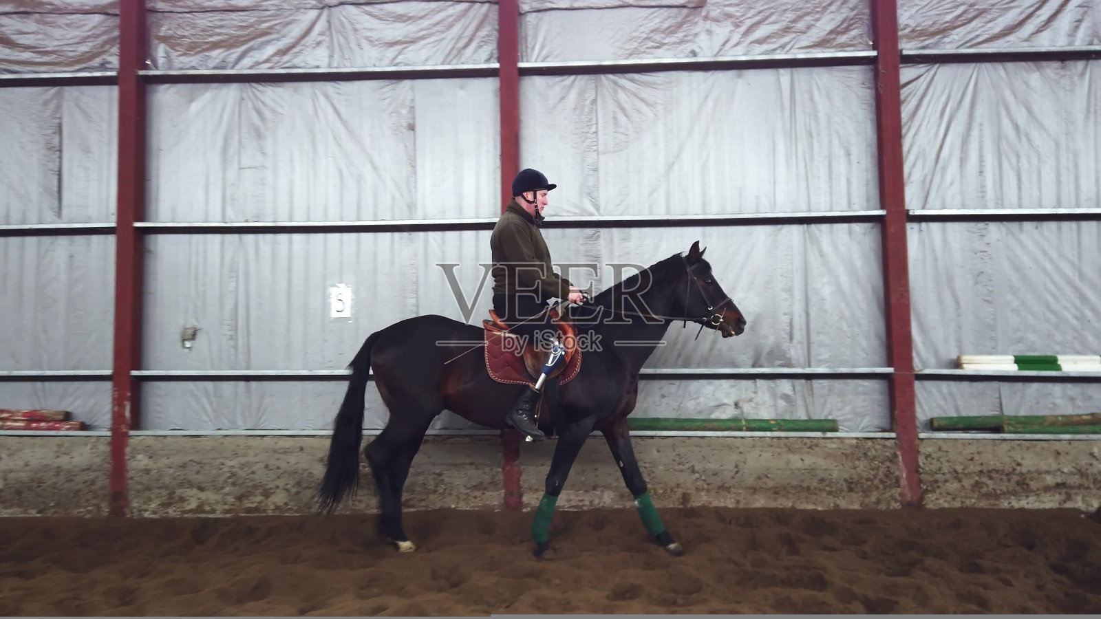 特别机库中学习骑黑色纯种马的年轻残疾男人(康复疗法)。该男人的右腿是假肢。照片摄影图片