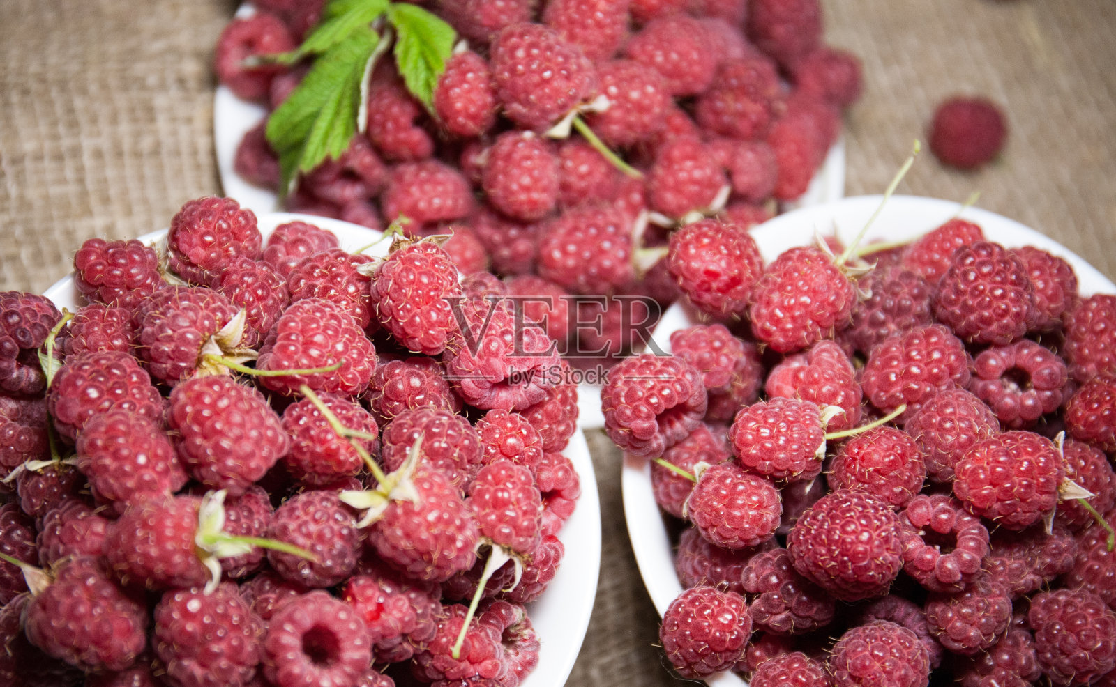 成熟的甜覆盆子放在白色的碗里,粗麻布做背景。特写镜头照片摄影图片