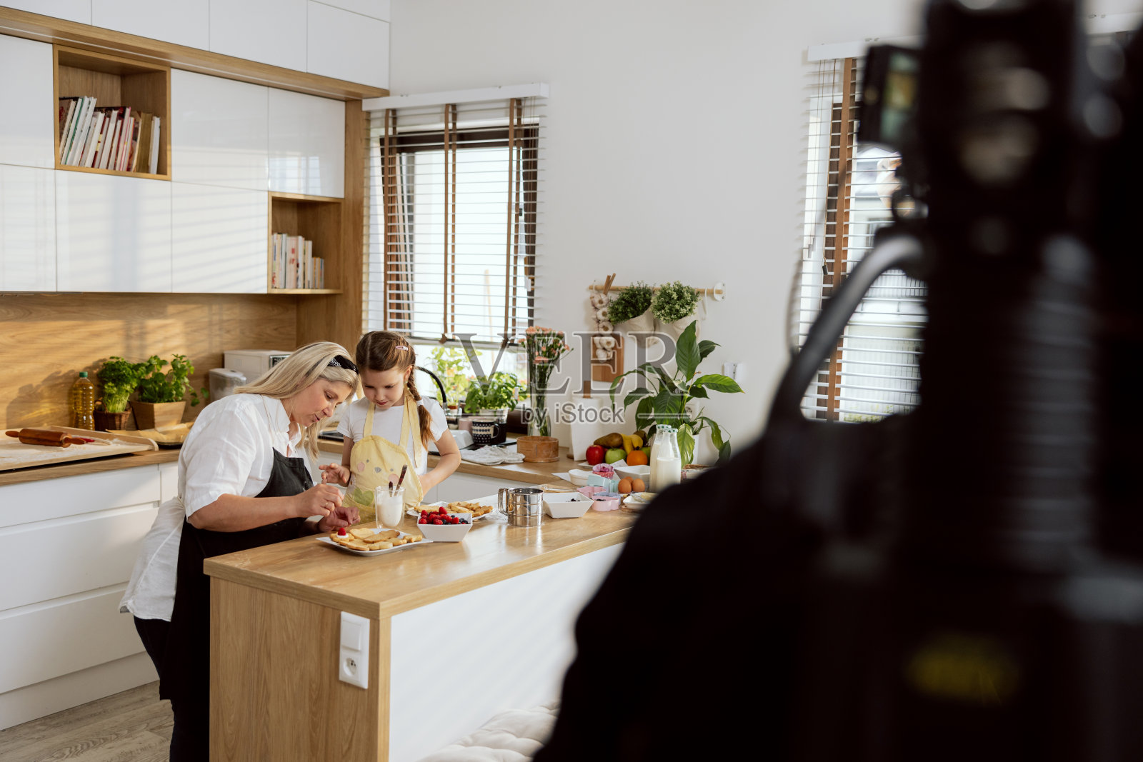 奶奶和孙子一边录制烹饪节目,一边在厨房烘焙饼干。在电视节目中拍摄关于烘焙饼干的视频照片摄影图片