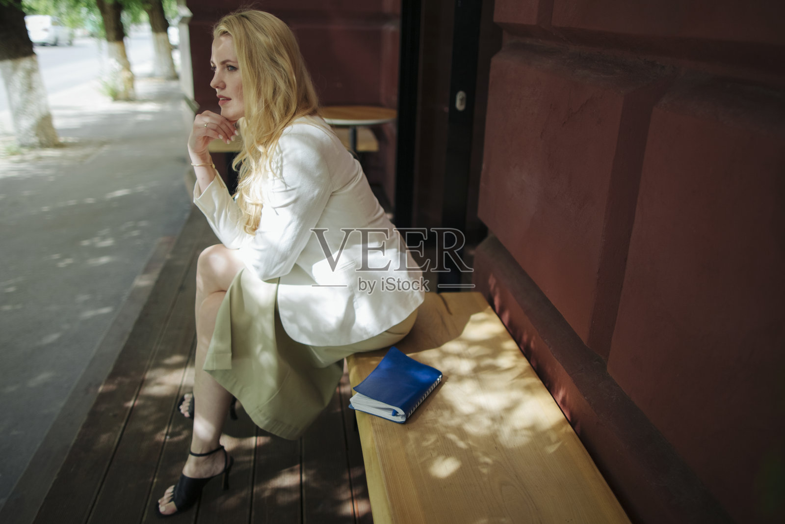 一位穿着白色西装、拿着记事本的女商人坐在一家夏季咖啡馆附近的长椅上冥想照片摄影图片