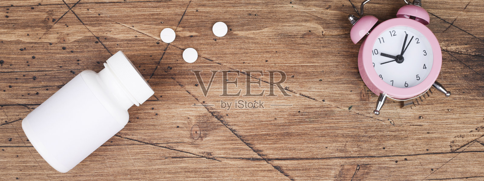 女性健康的概念。医药、保健风格。副本的空间。白色塑料瓶与药片和时钟在棕色的木头背景。横幅复制空间照片摄影图片