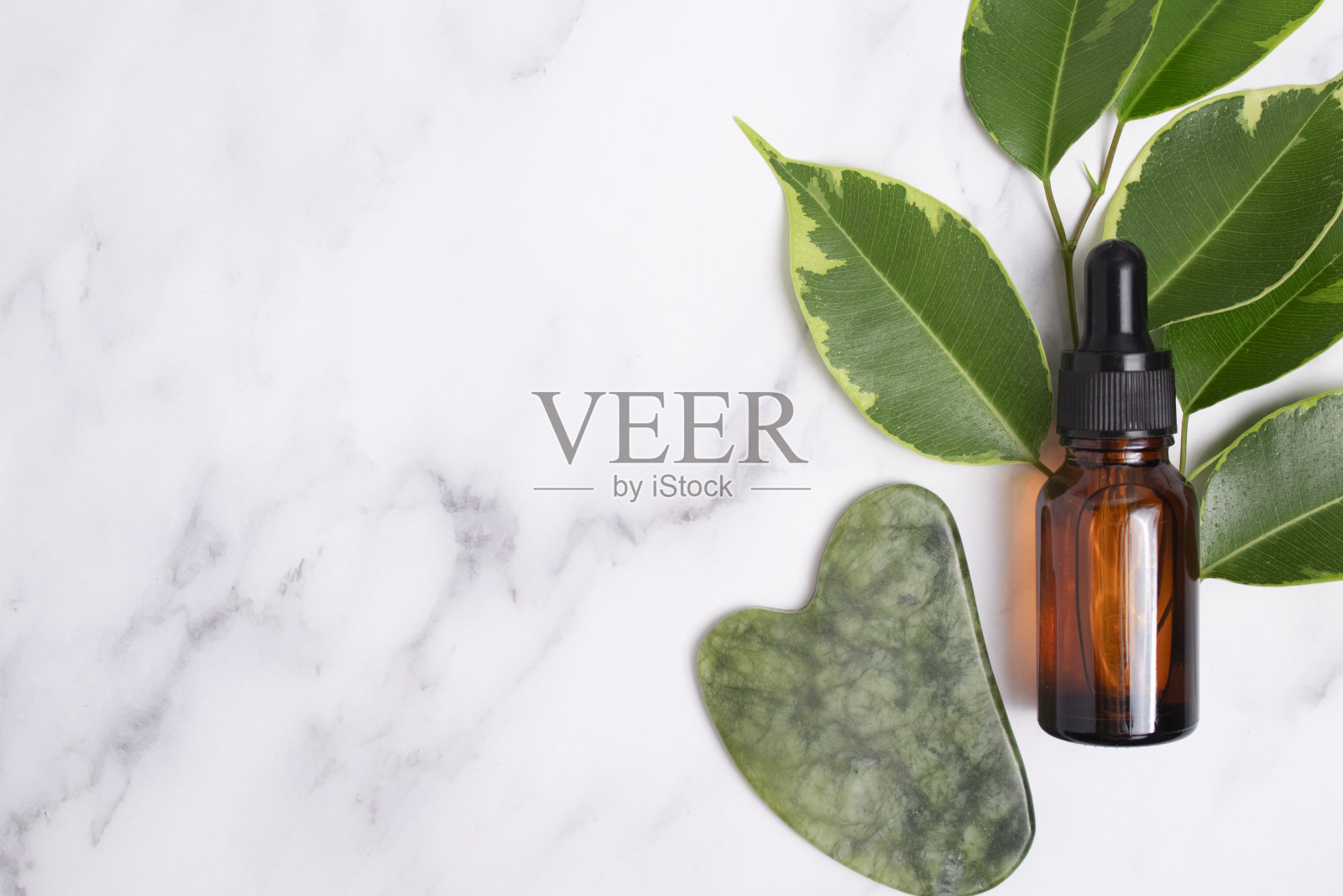 无烙印血清瓶,挂沙,大理石背景上的叶子。玉面按摩器用于面部按摩治疗。抗衰老、提容、调理照片摄影图片