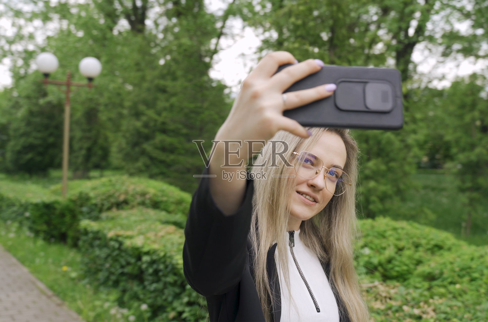 快乐的调情年轻女孩在公园里用智能手机拍了一张自己的照片。照片摄影图片