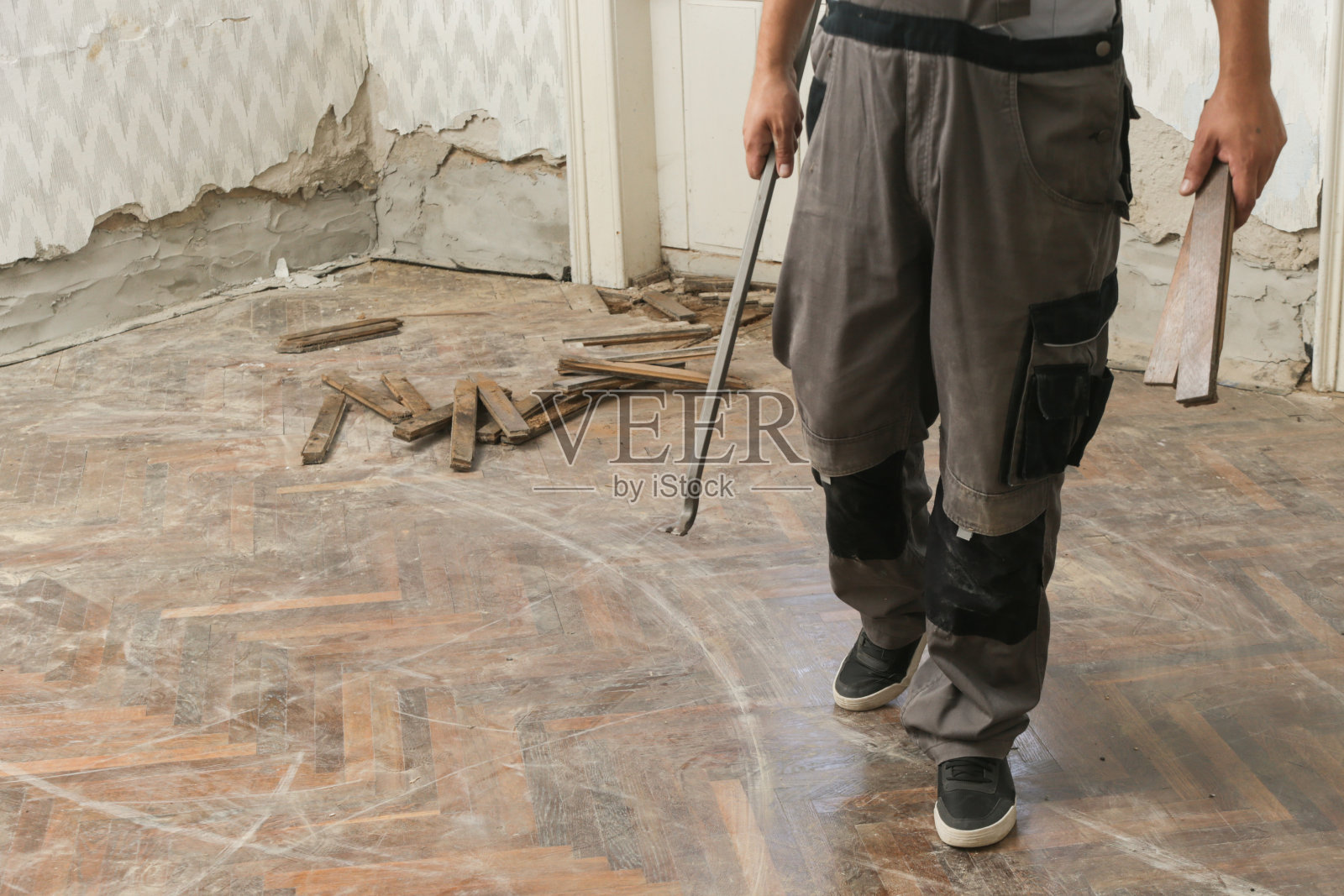 家居装饰。建筑工人或勤杂工正在用撬棍工具拆除旧的木制拼花地板。旧木地板翻新。照片摄影图片