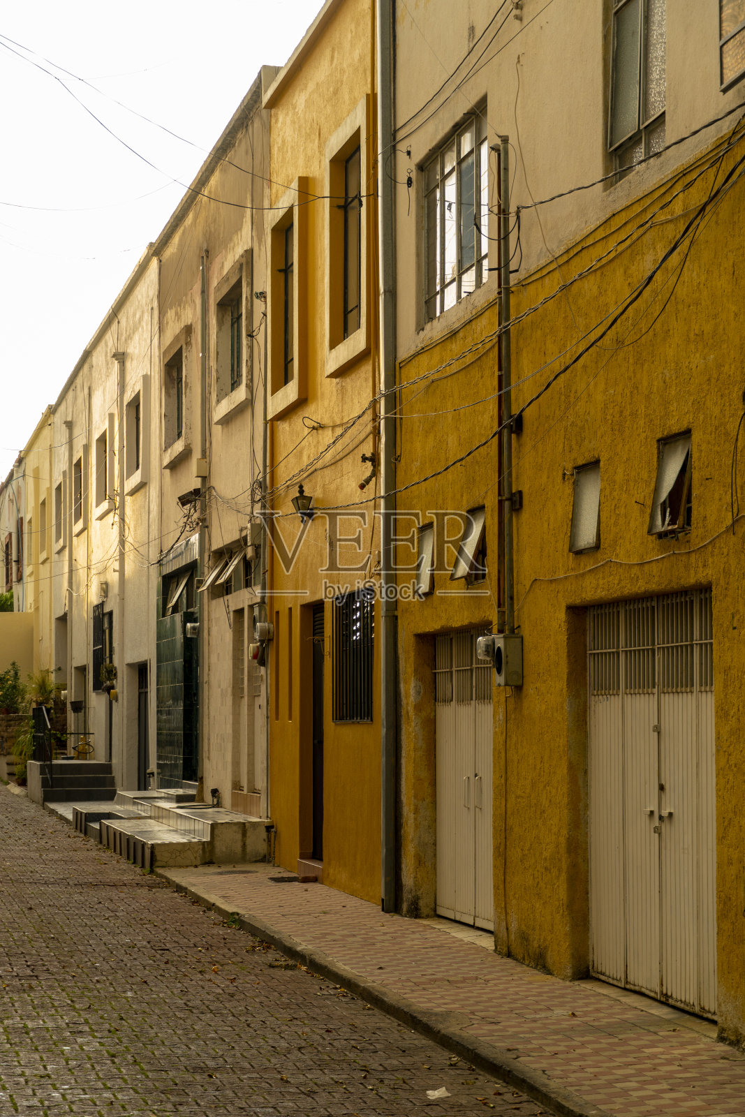 日落时分,一个小社区的车道、人行道和鹅卵石,毗邻黄色和芥末色的房屋照片摄影图片