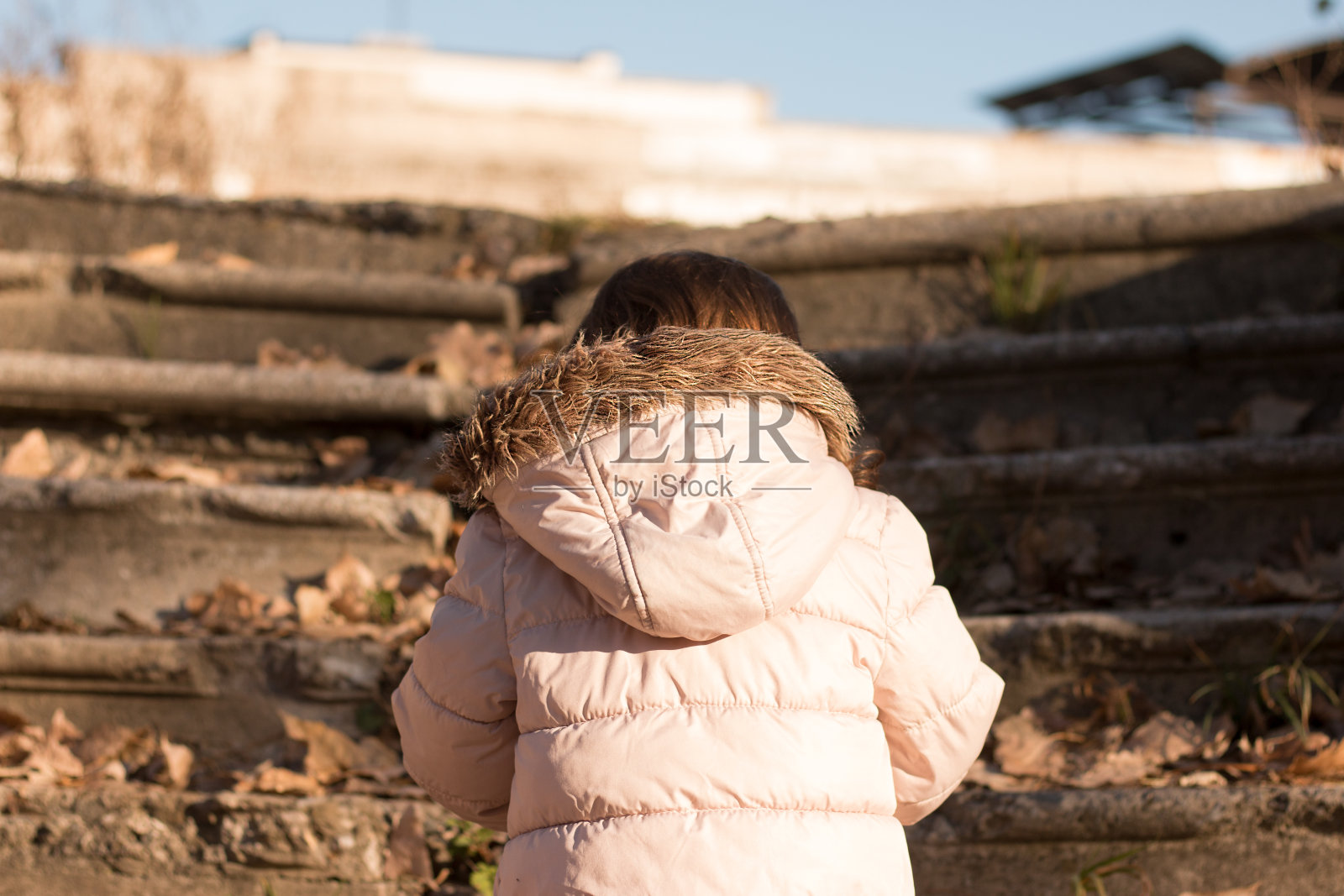 一个红头发的孩子穿着夹克,戴着蓬松的兜帽,走在秋天肮脏的公园里照片摄影图片
