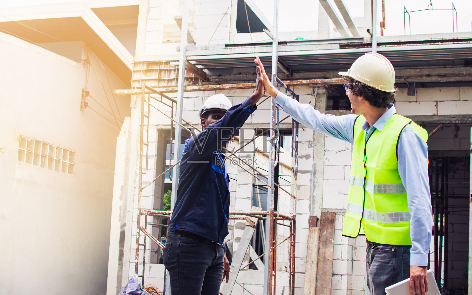 两名多元化的男性工程师在施工现场进行户外检查,戴着安全帽,与获胜者和成功人士击掌、握手。职业,行业的概念。照片摄影图片