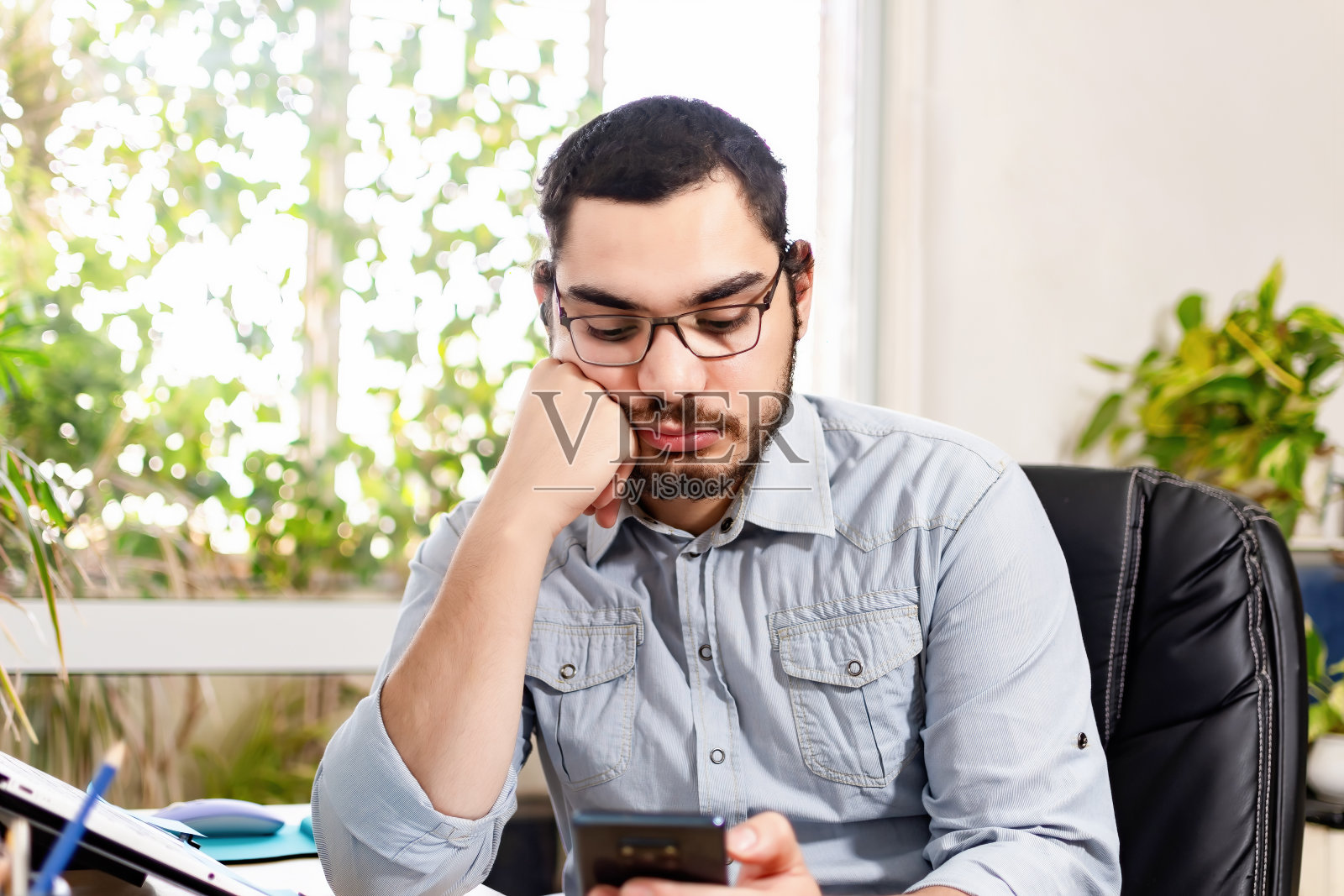 无聊的高管一边在办公桌上工作一边使用智能手机。照片摄影图片