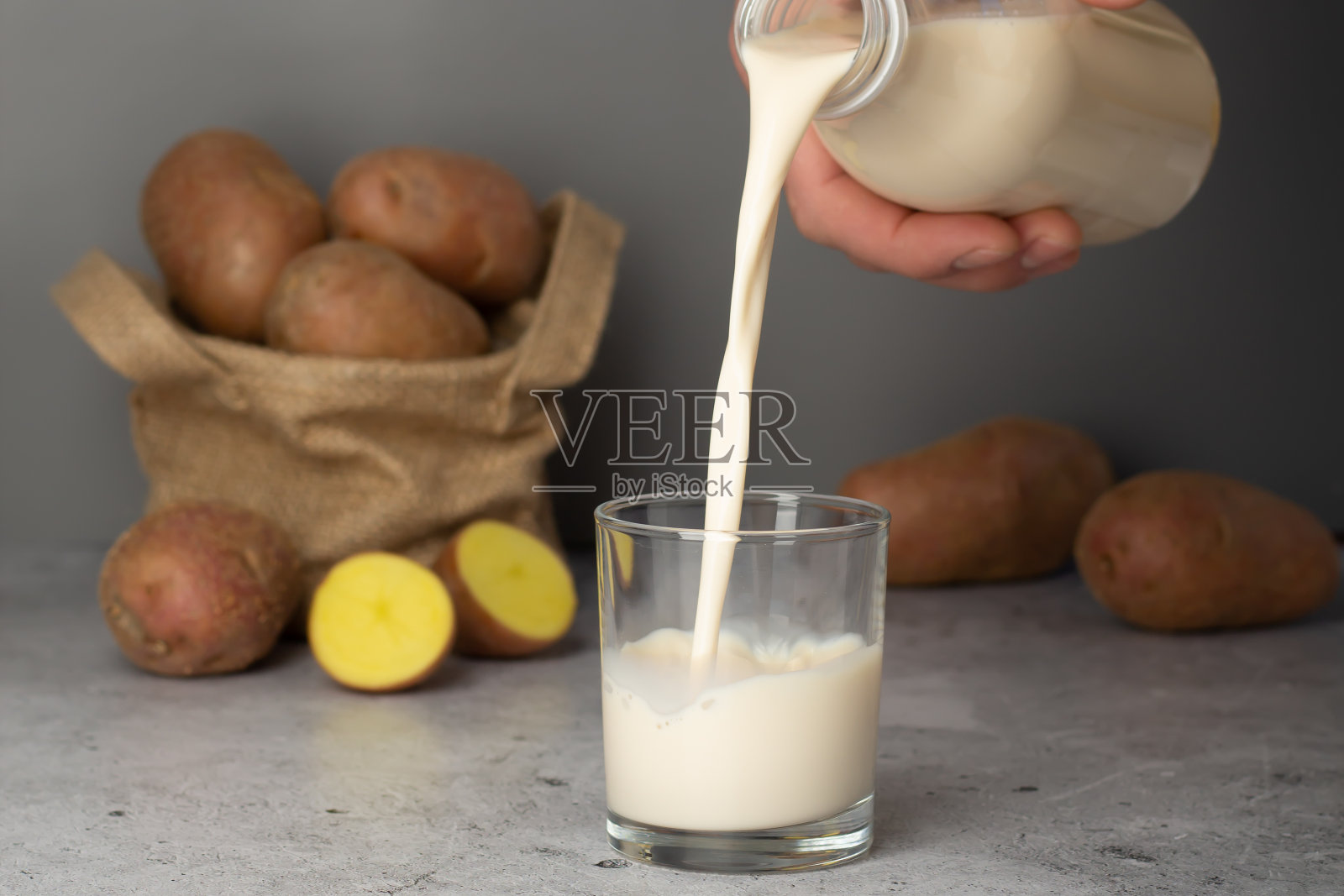 用男子的手把土豆牛奶倒进杯子里。照片摄影图片